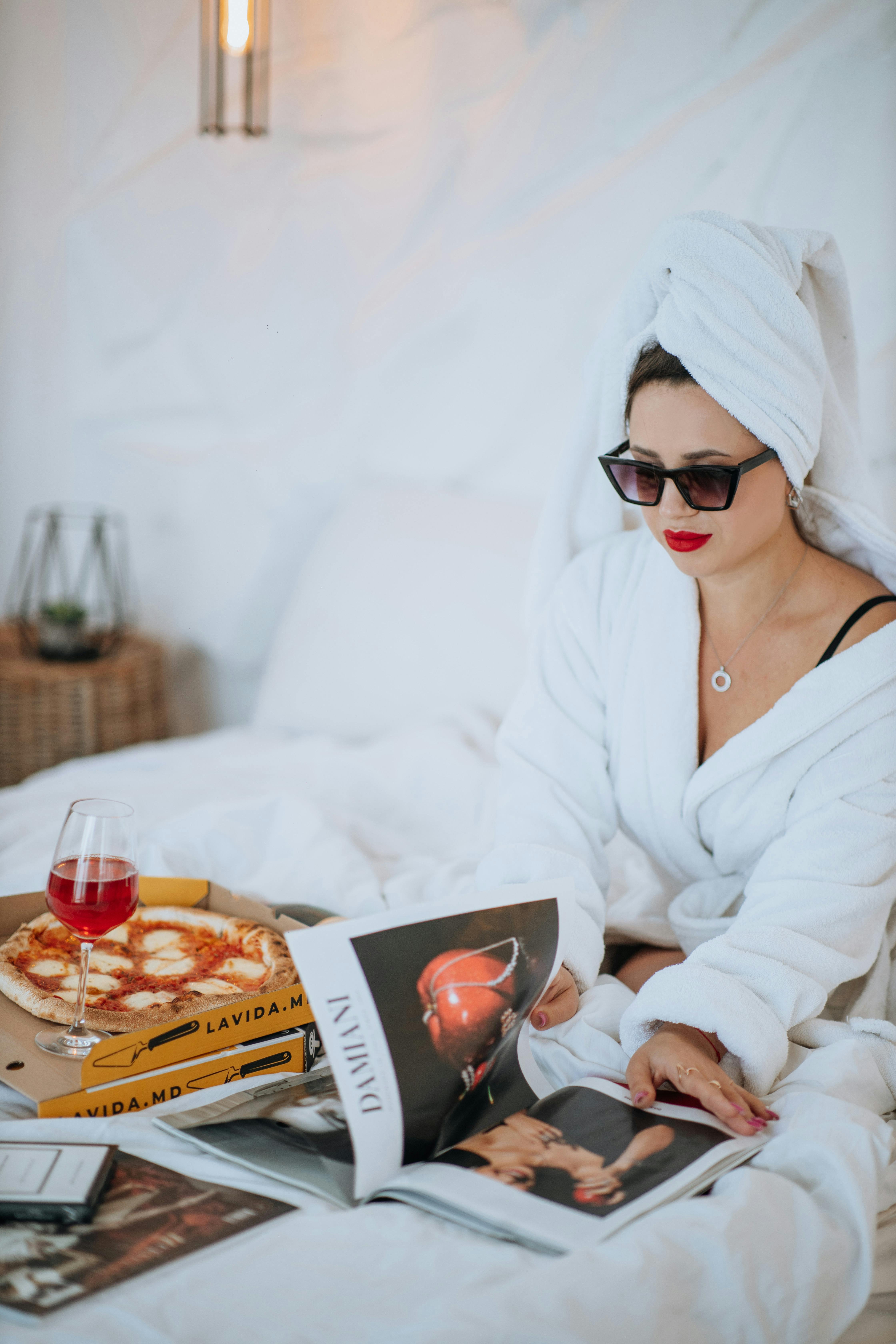 Une femme en peignoir mangeant une pizza au lit | Source : Pexels
