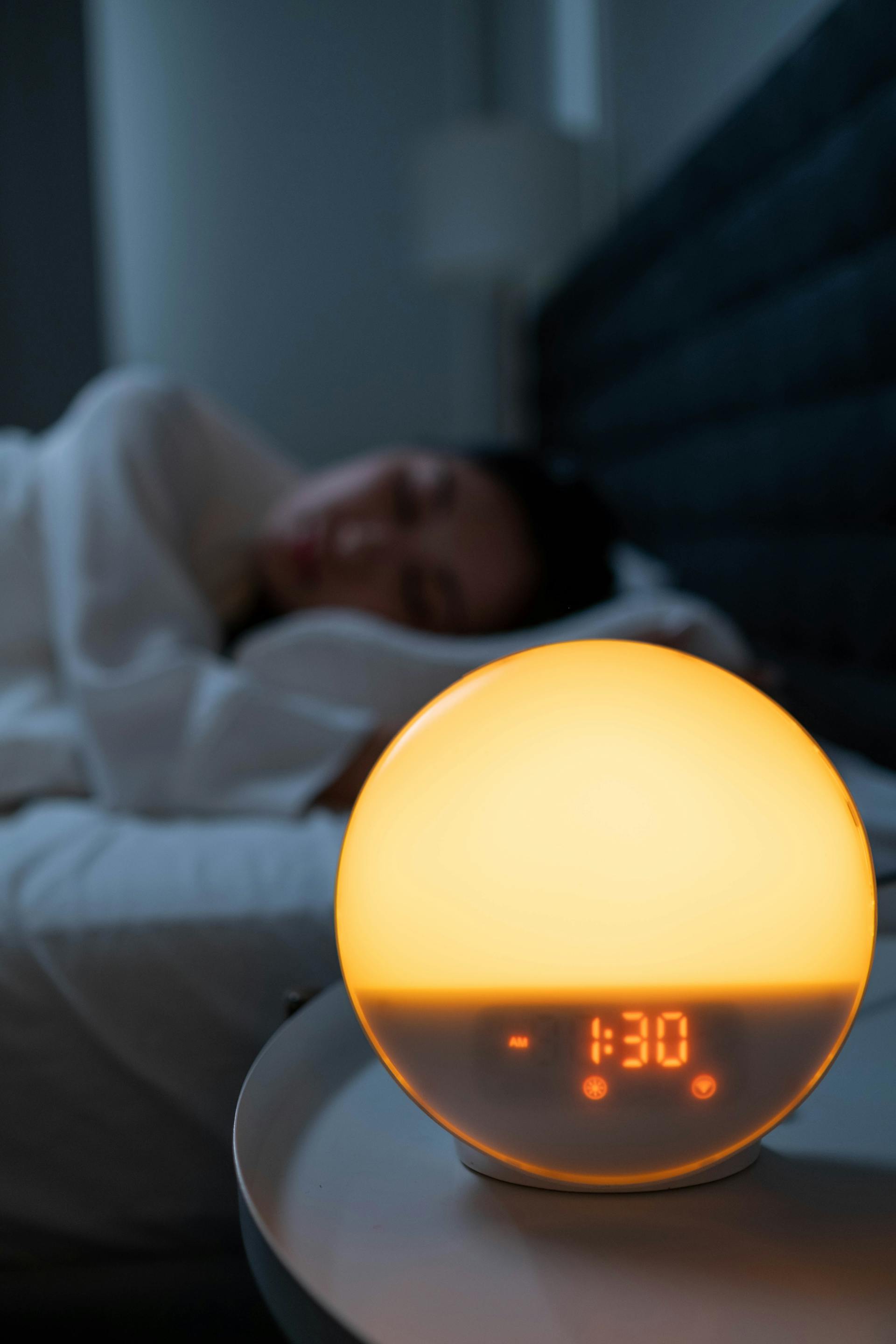 Une horloge sur une table de nuit avec une femme qui dort en arrière-plan | Source : Pexels