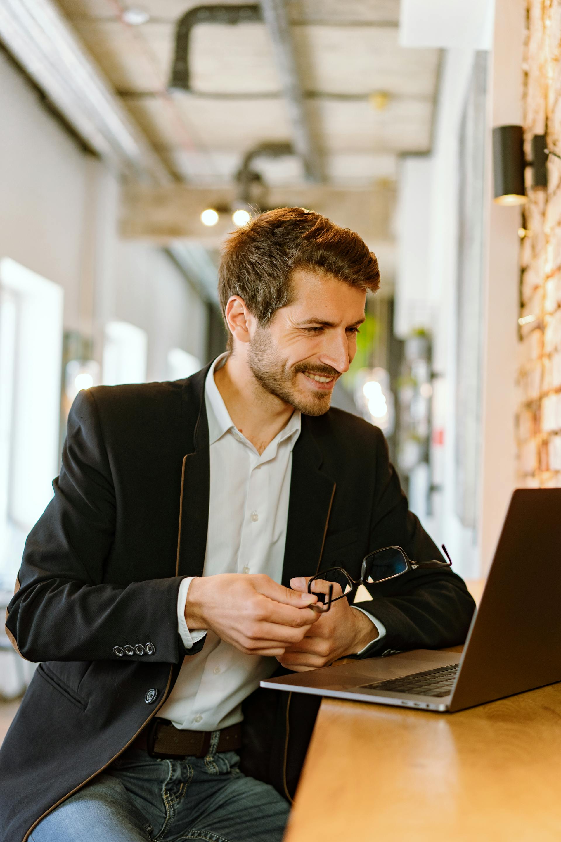 Un homme en costume sourit en regardant son ordinateur portable | Source : Pexels