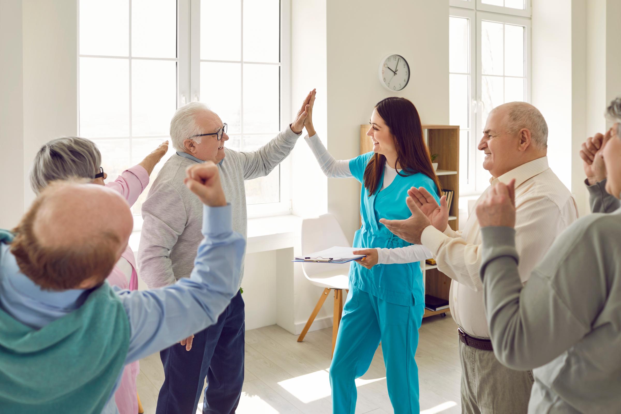 Une infirmière sympathique donnant un « high five » à des personnes âgées dans une maison de retraite | Source : Shutterstock