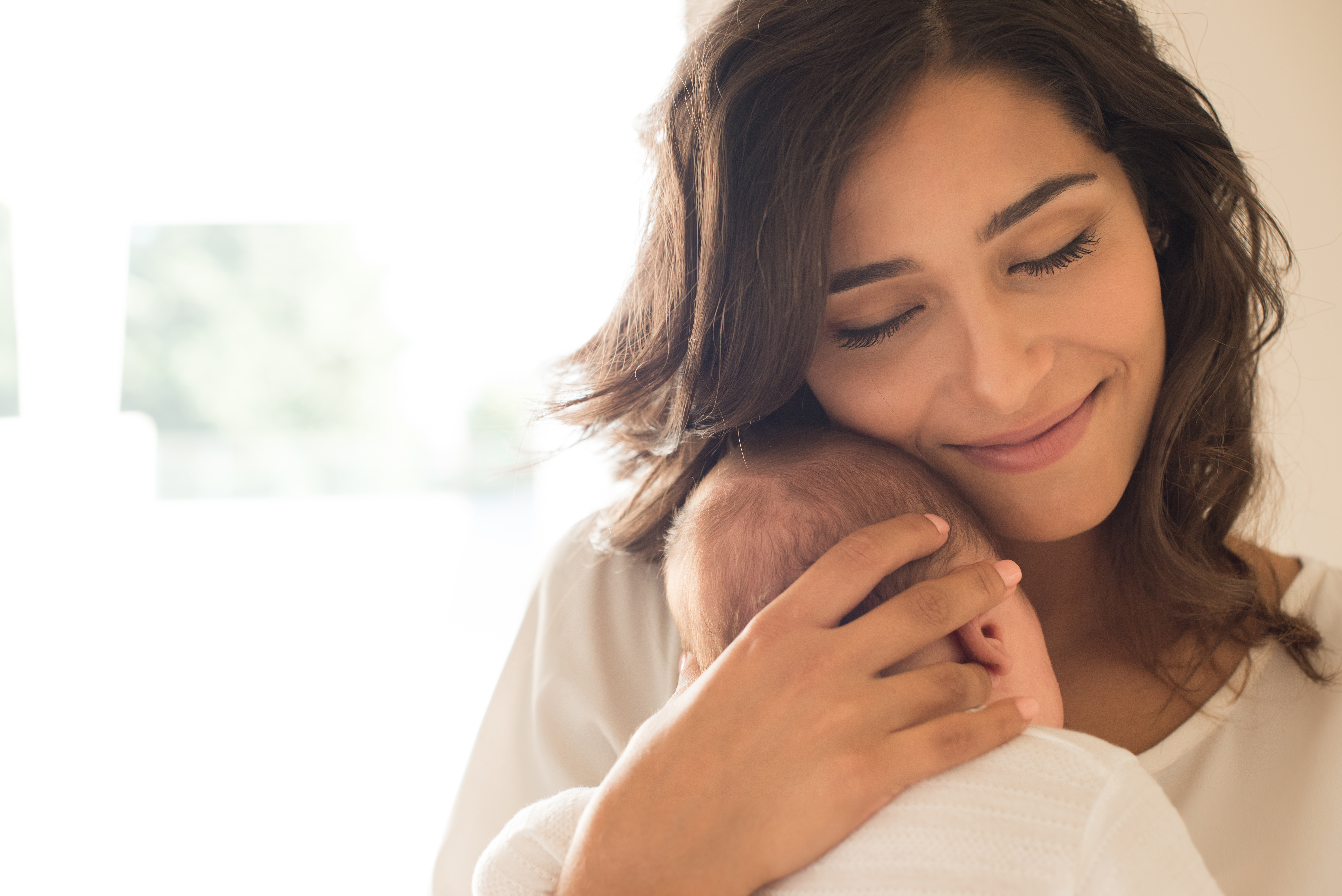 Une mère sourit tout en blottissant son bébé contre sa poitrine | Source : Shutterstock