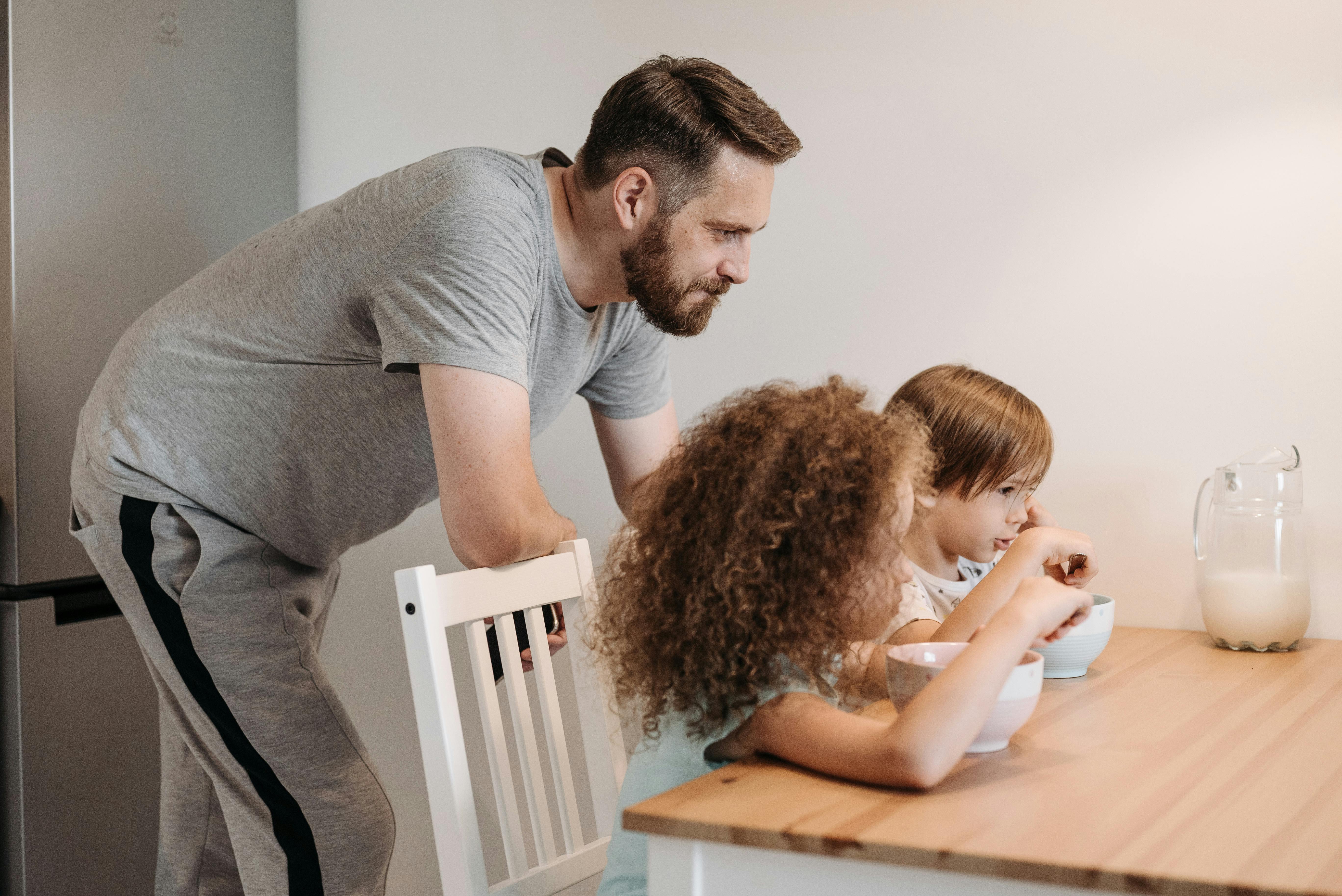 Un père qui regarde ses deux filles prendre leur petit déjeuner | Source : Pexels