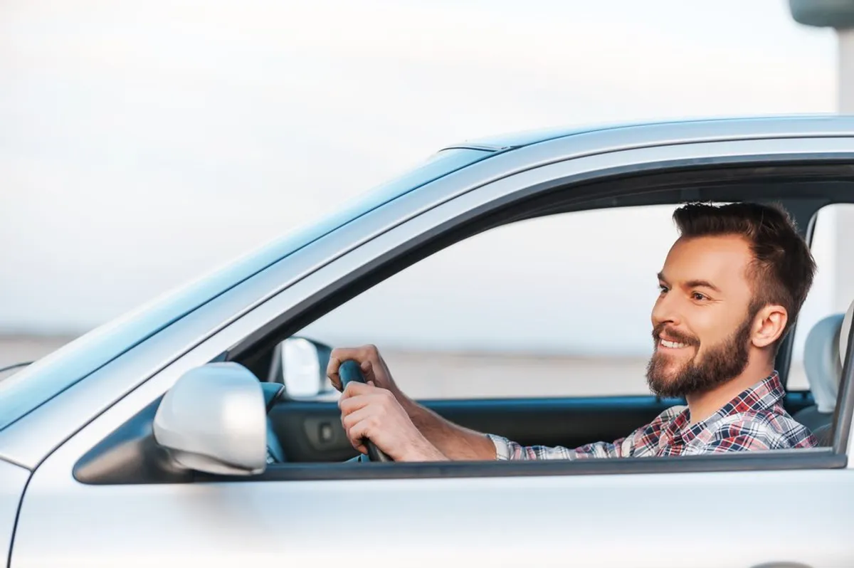 La photo d'un jeune homme souriant au volant de sa voiture. | Photo: Shutterstock