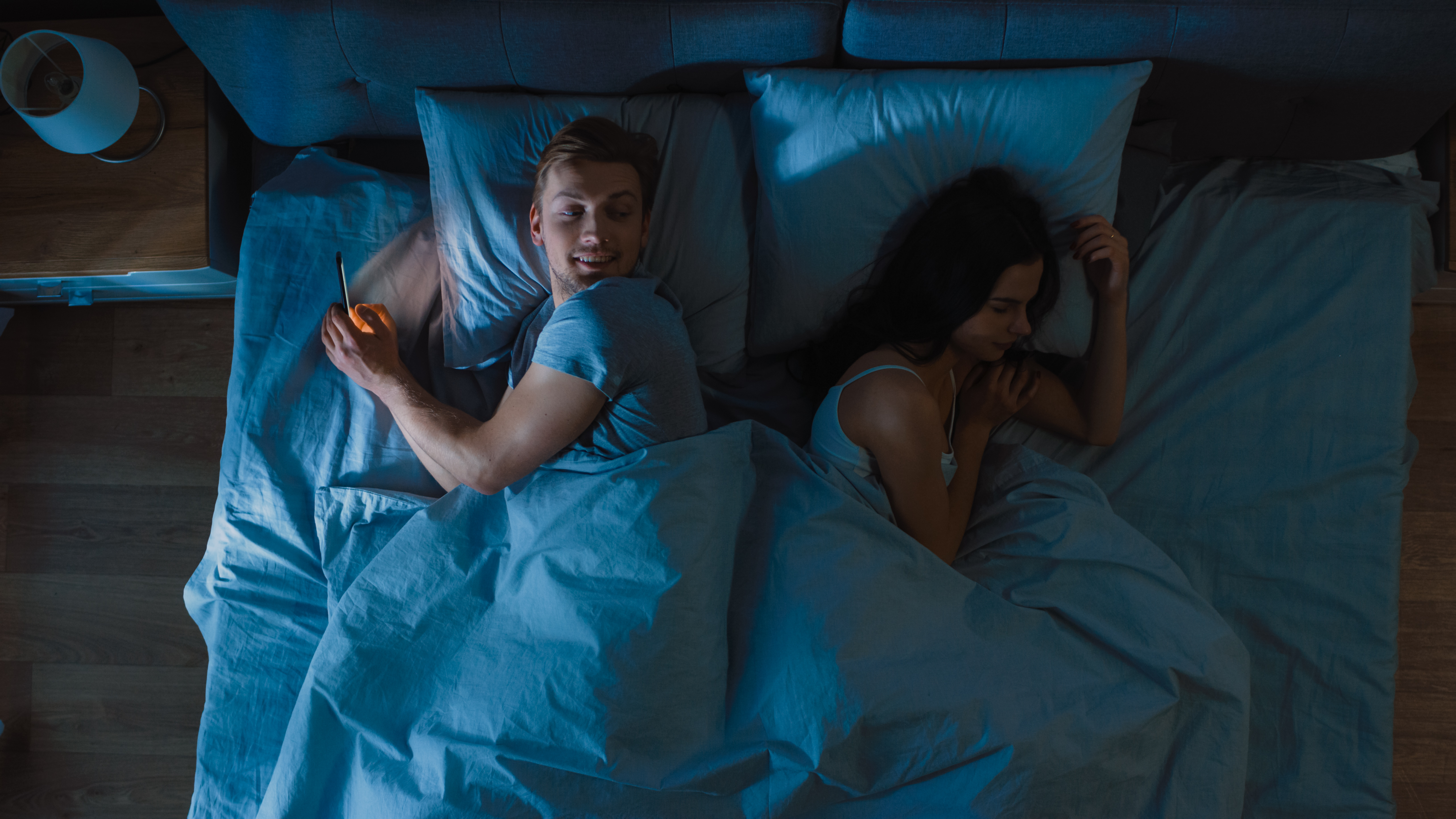 Un homme tourne le dos à sa femme au lit pour envoyer un texto à quelqu'un d'autre | Source : Shutterstock