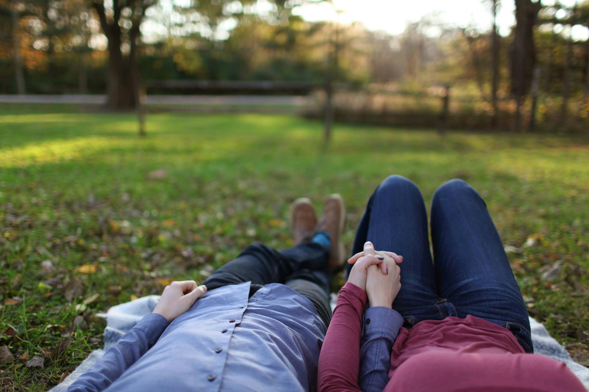 Un couple allongé dans l'herbe tout en se tenant par la main | Source : Pexels
