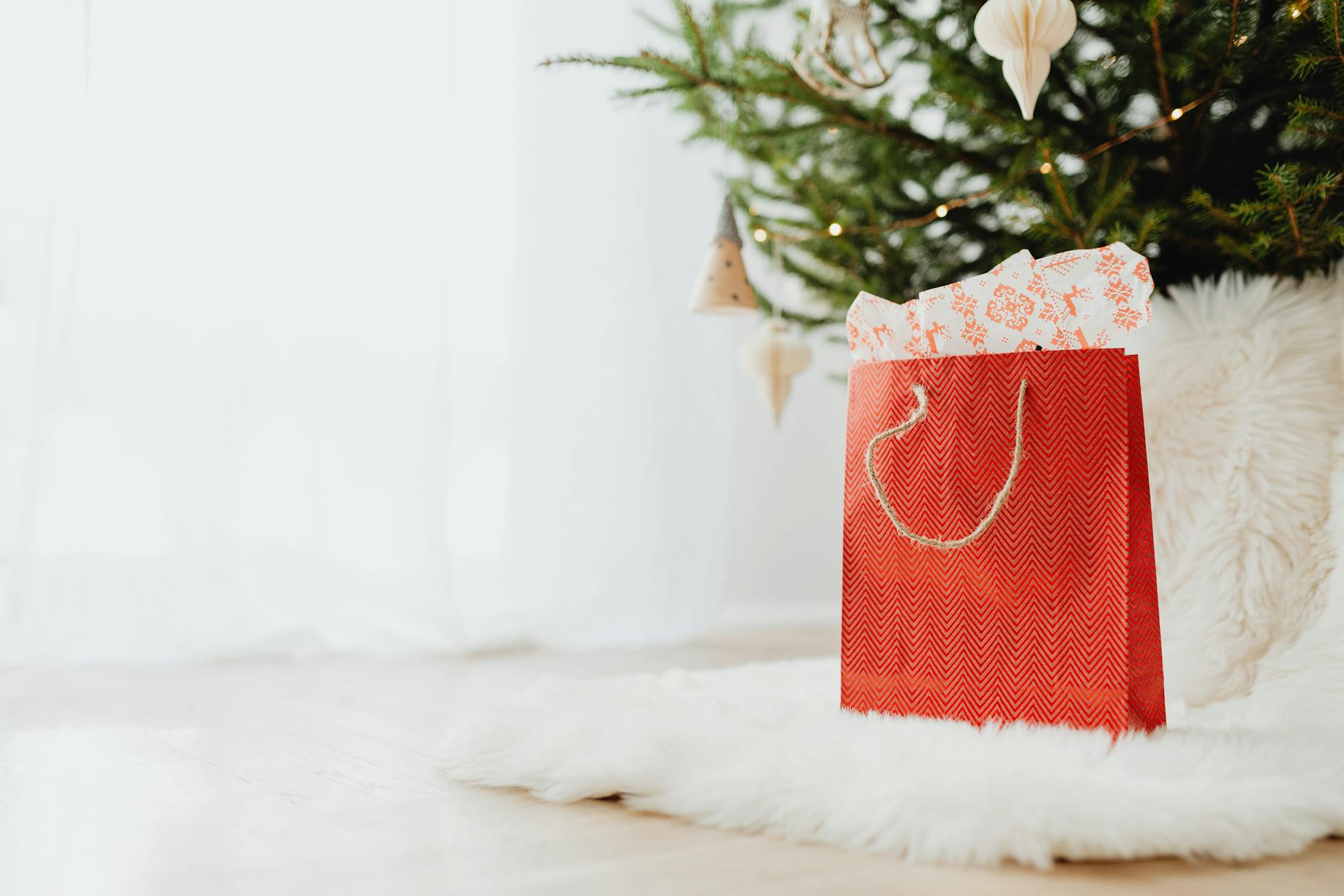 Un sac cadeau rouge posé sur un tapis de fourrure blanche | Source : Pexels