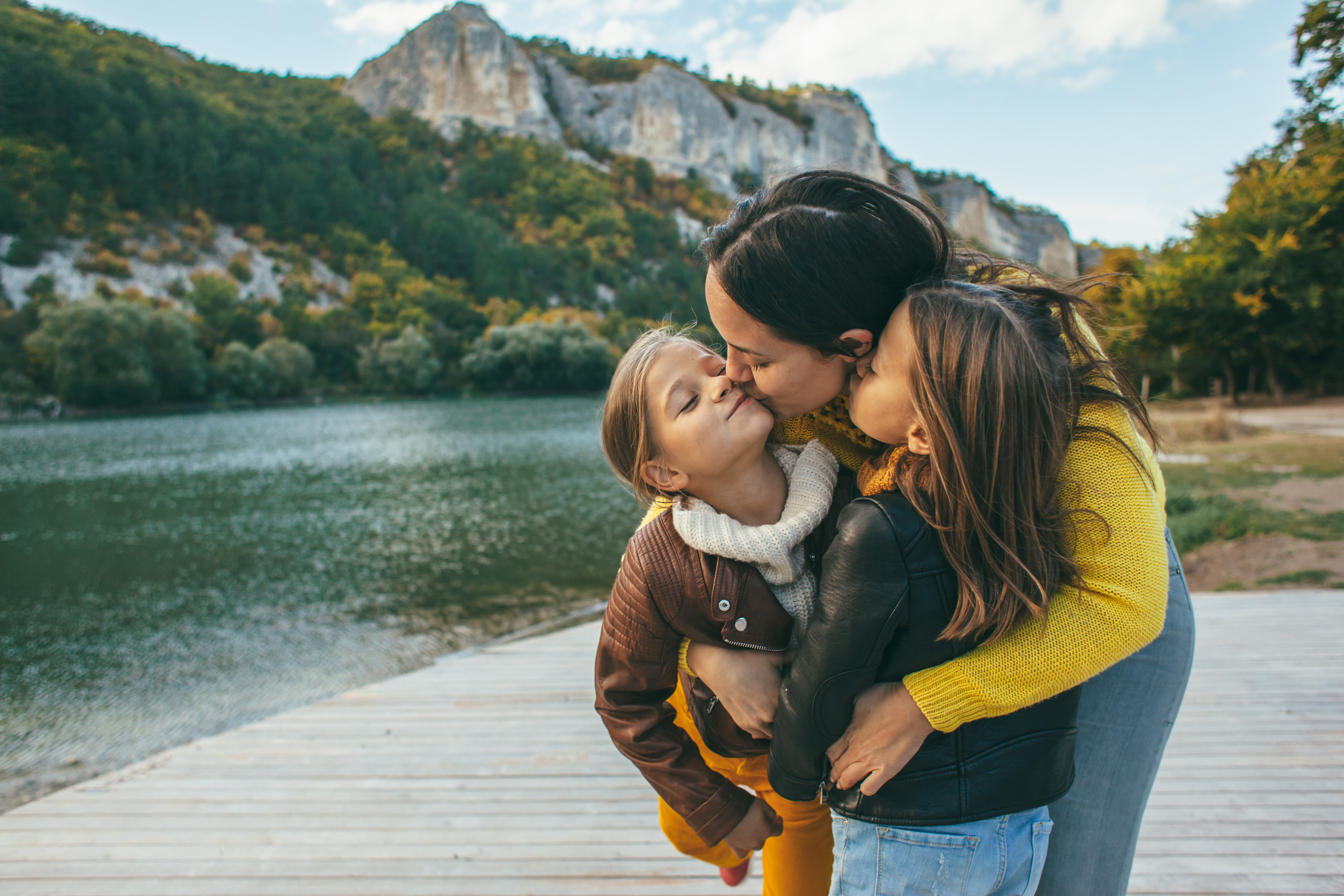 Une femme embrasse ses petites filles près d'un étang | Source : Shutterstock