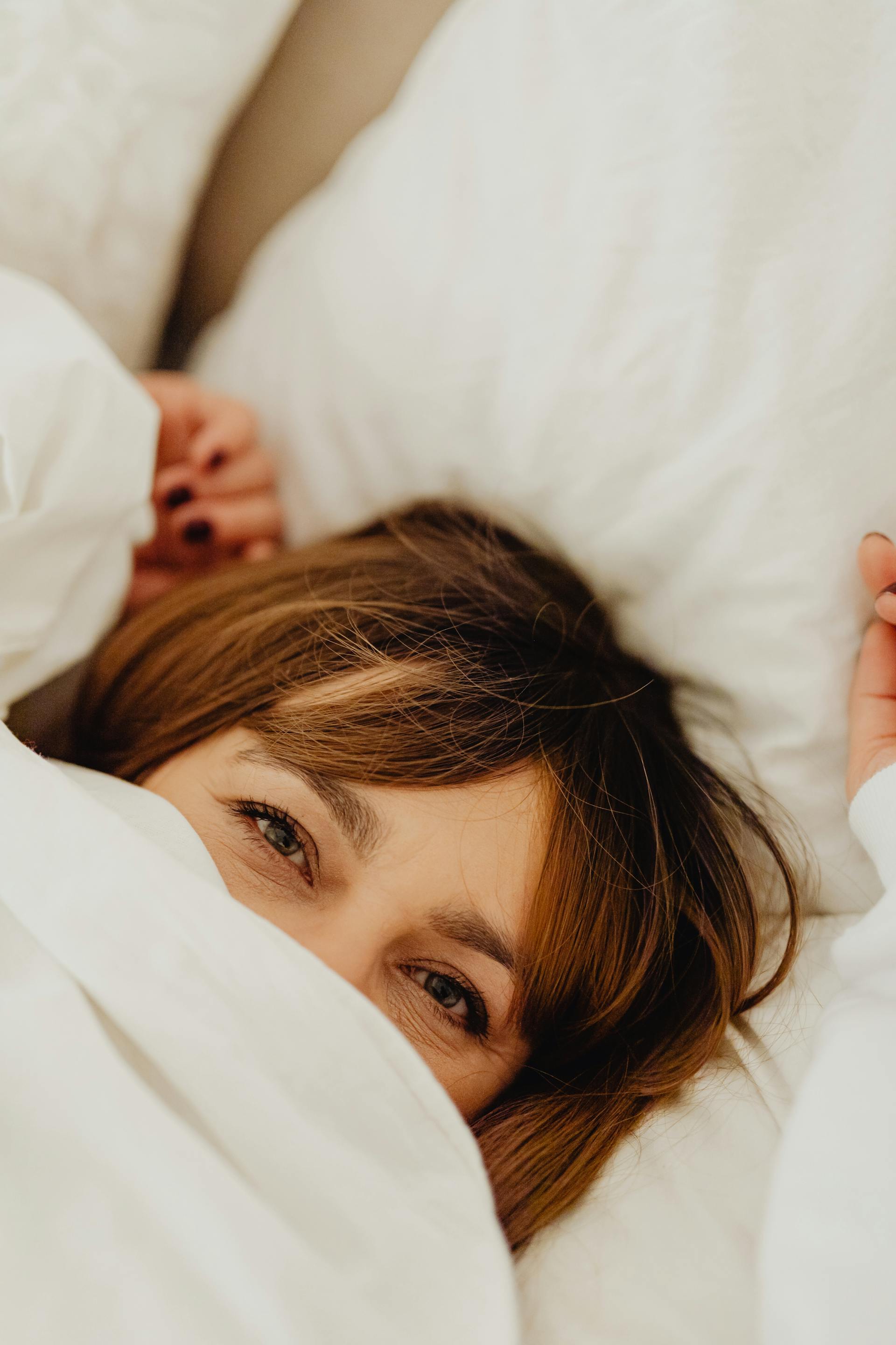 Une femme allongée dans son lit, le visage caché sous une couverture blanche | Source : Pexels