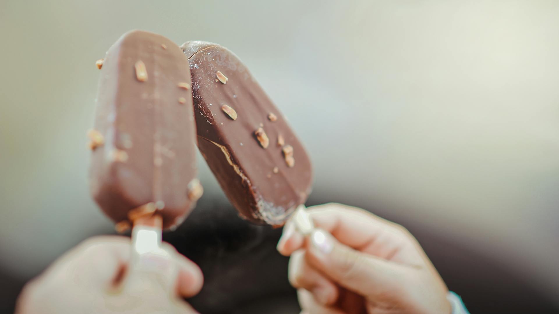 Gros plan de deux mains tenant des bâtonnets de glace au chocolat | Source : Pexels