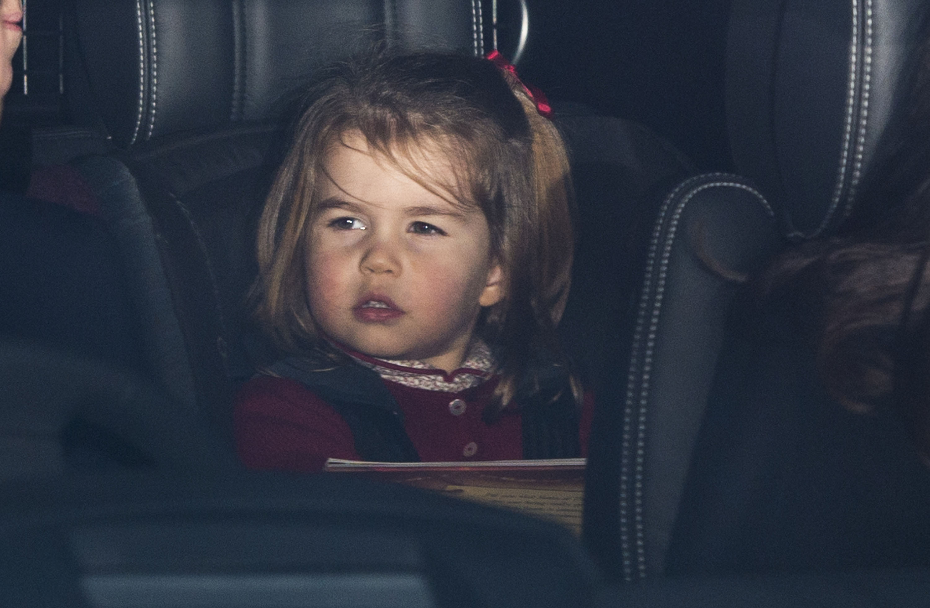 La princesse Charlotte de Cambridge jette un coup d'œil depuis la banquette arrière d'une voiture qui arrive pour le déjeuner annuel de Noël de la famille royale élargie au palais de Buckingham, le 20 décembre 2017, à Londres, en Angleterre. La jeune princesse porte un cardigan bordeaux de fête par-dessus un haut à col imprimé, et ses cheveux sont coiffés d'un nœud en ruban rouge assorti. | Source : Getty Images