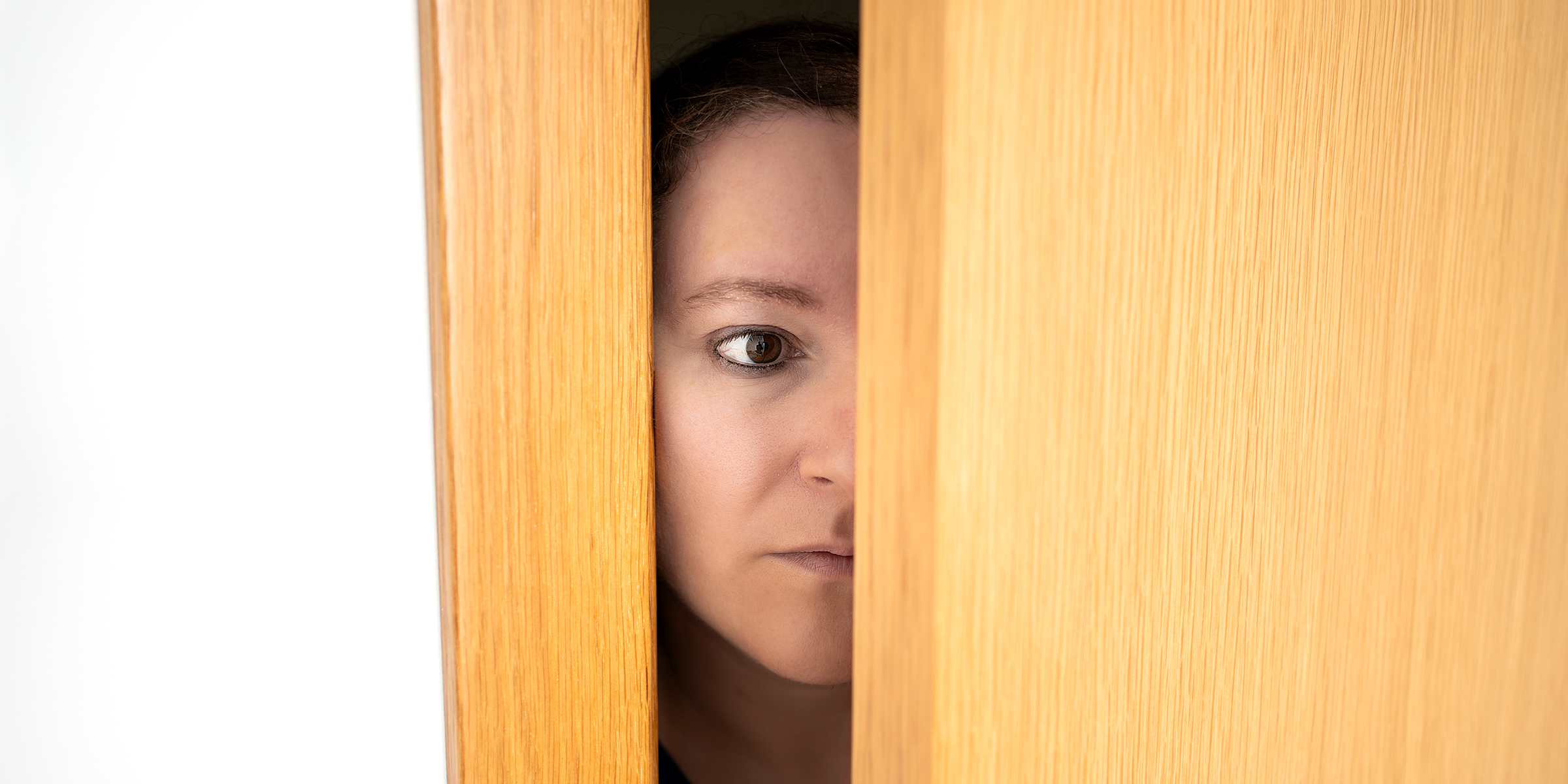 Une femme effrayée écoutant aux portes derrière une porte | Source : Shutterstock