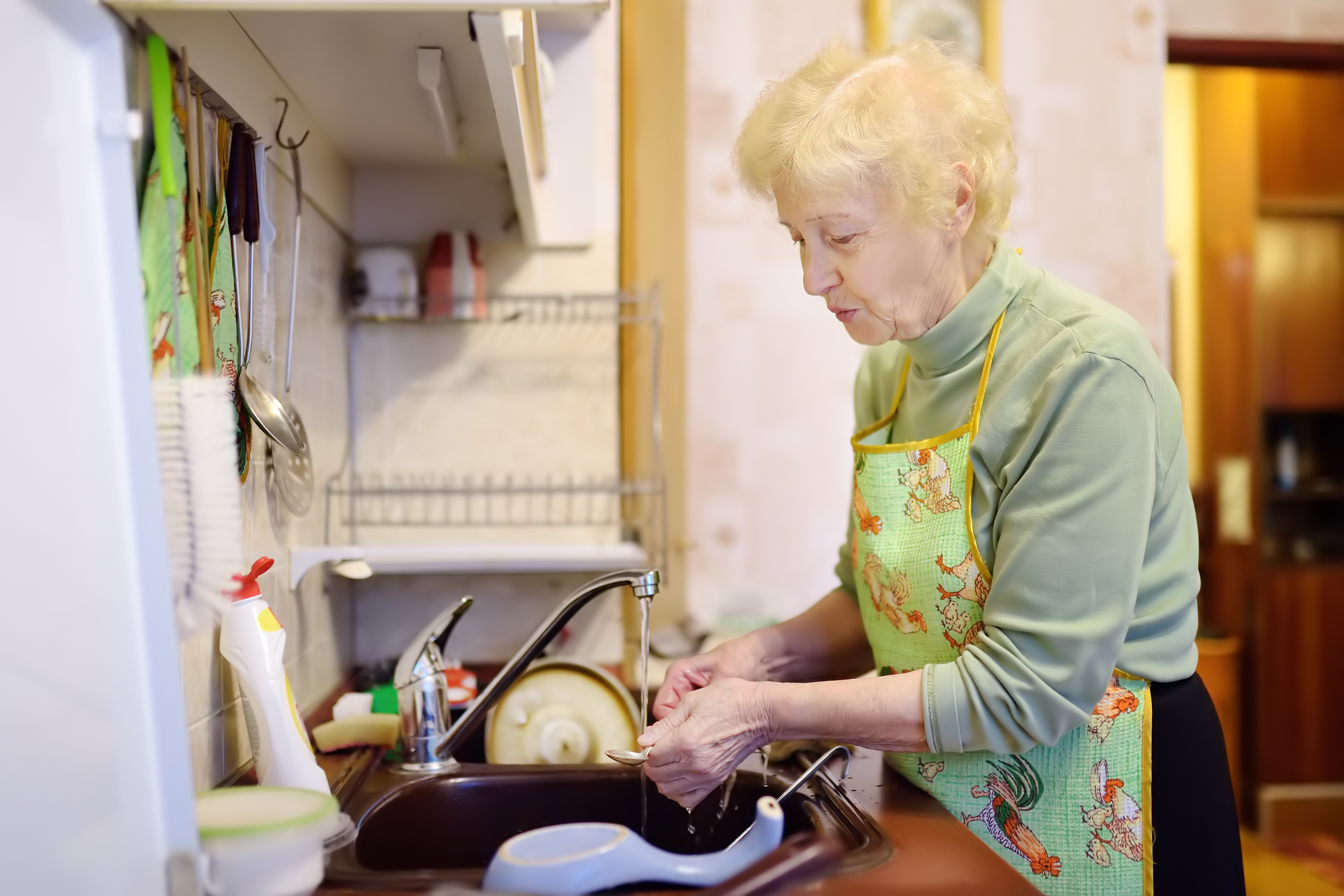 Une dame âgée fait la vaisselle dans la cuisine | Source : Shutterstock