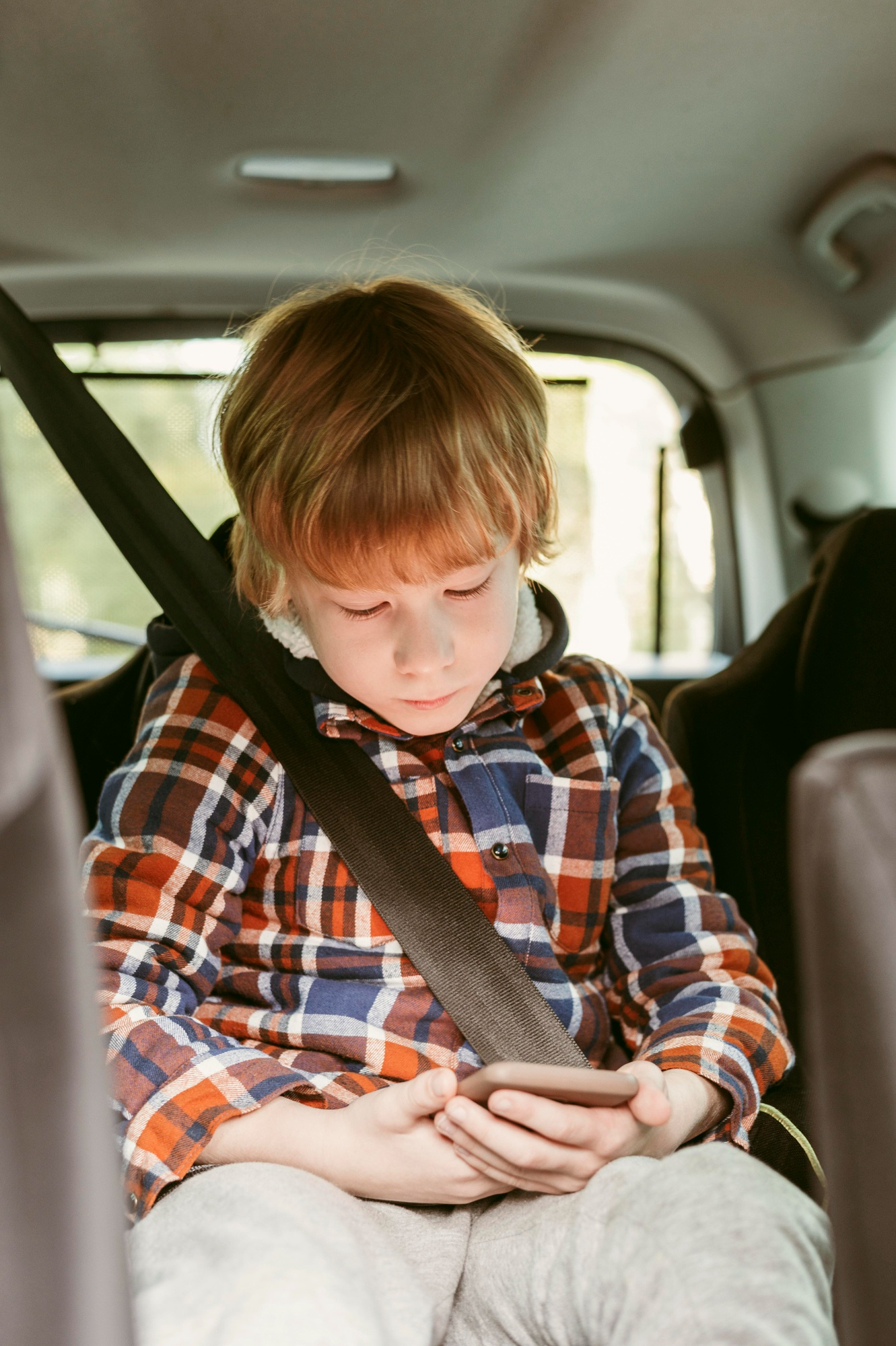 Un petit garçon concentré sur un téléphone à l'arrière d'une voiture | Source : Freepik