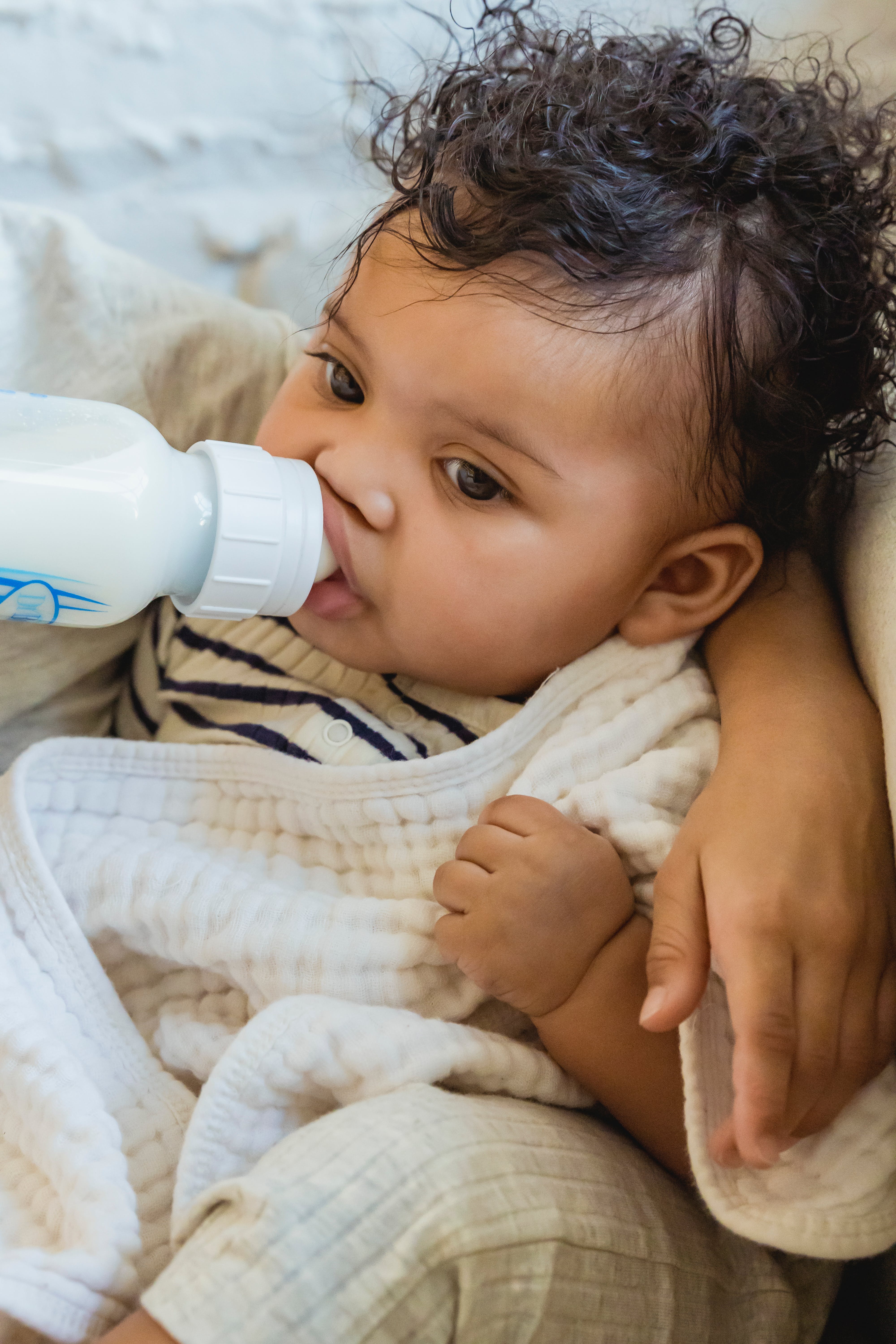 Un bébé tétant le lait d'un biberon alors qu'il est recouvert d'une couverture | Source : Pexels