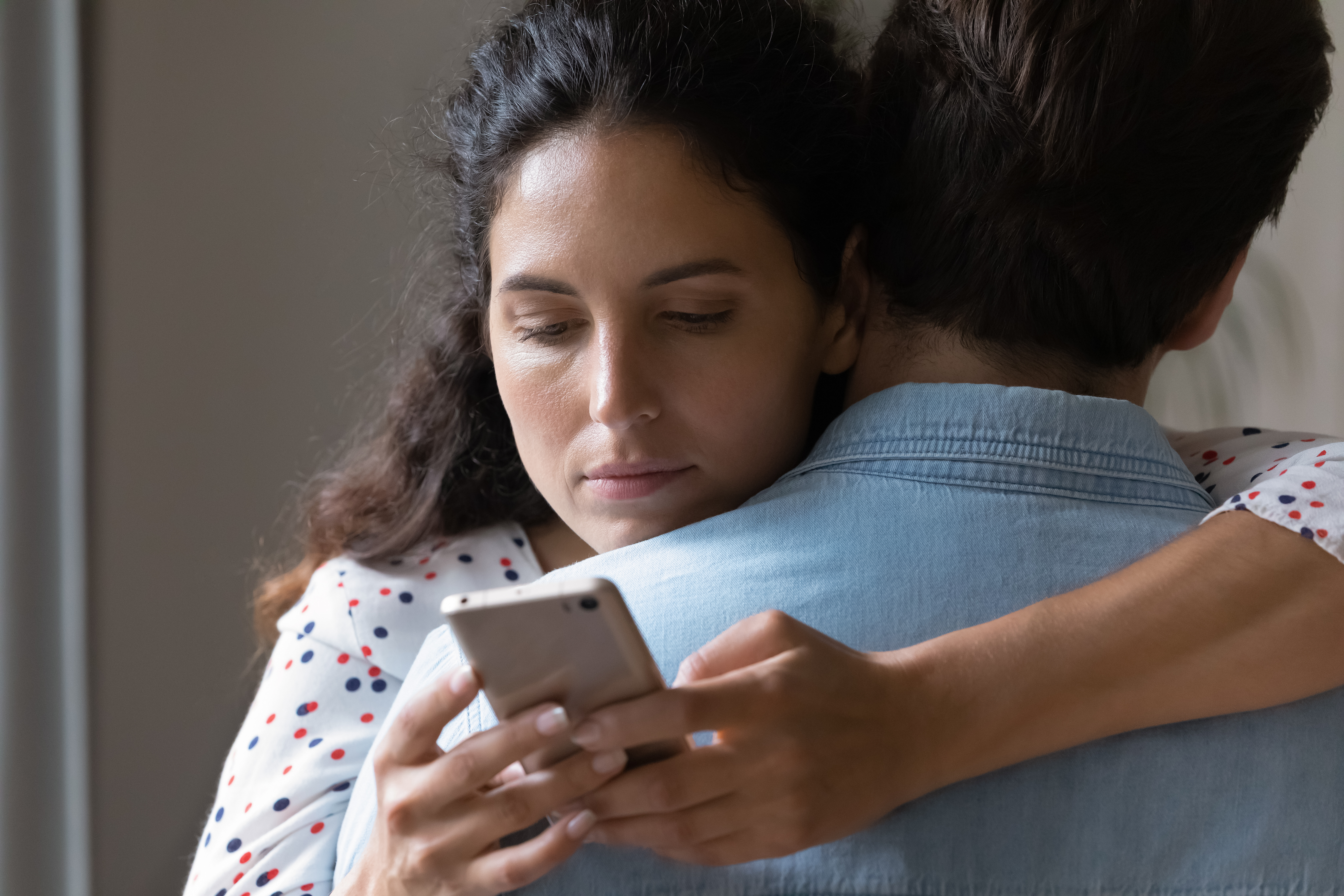 Un homme et une femme se serrant dans les bras tandis qu'elle regarde son téléphone dans son dos | Source : Shutterstock