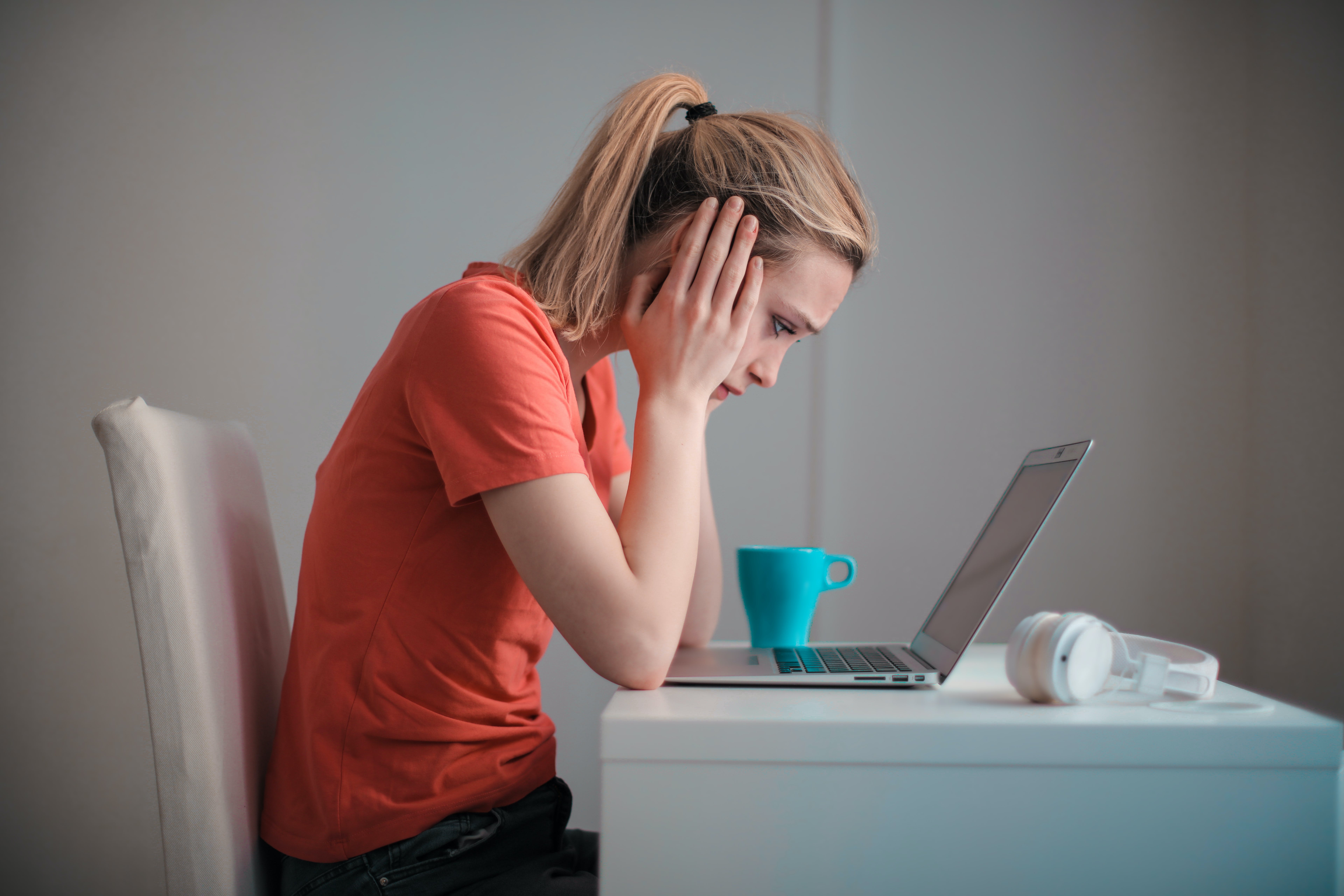 Une femme bouleversée, assise à un bureau, se tenant la main tout en regardant un ordinateur portable | Source : Pexels