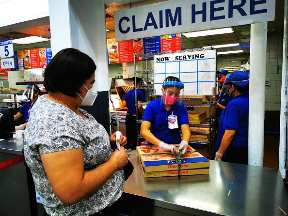 Une femme portant un masque facial achète une pizza dans un supermarché. |Photo : Getty Images