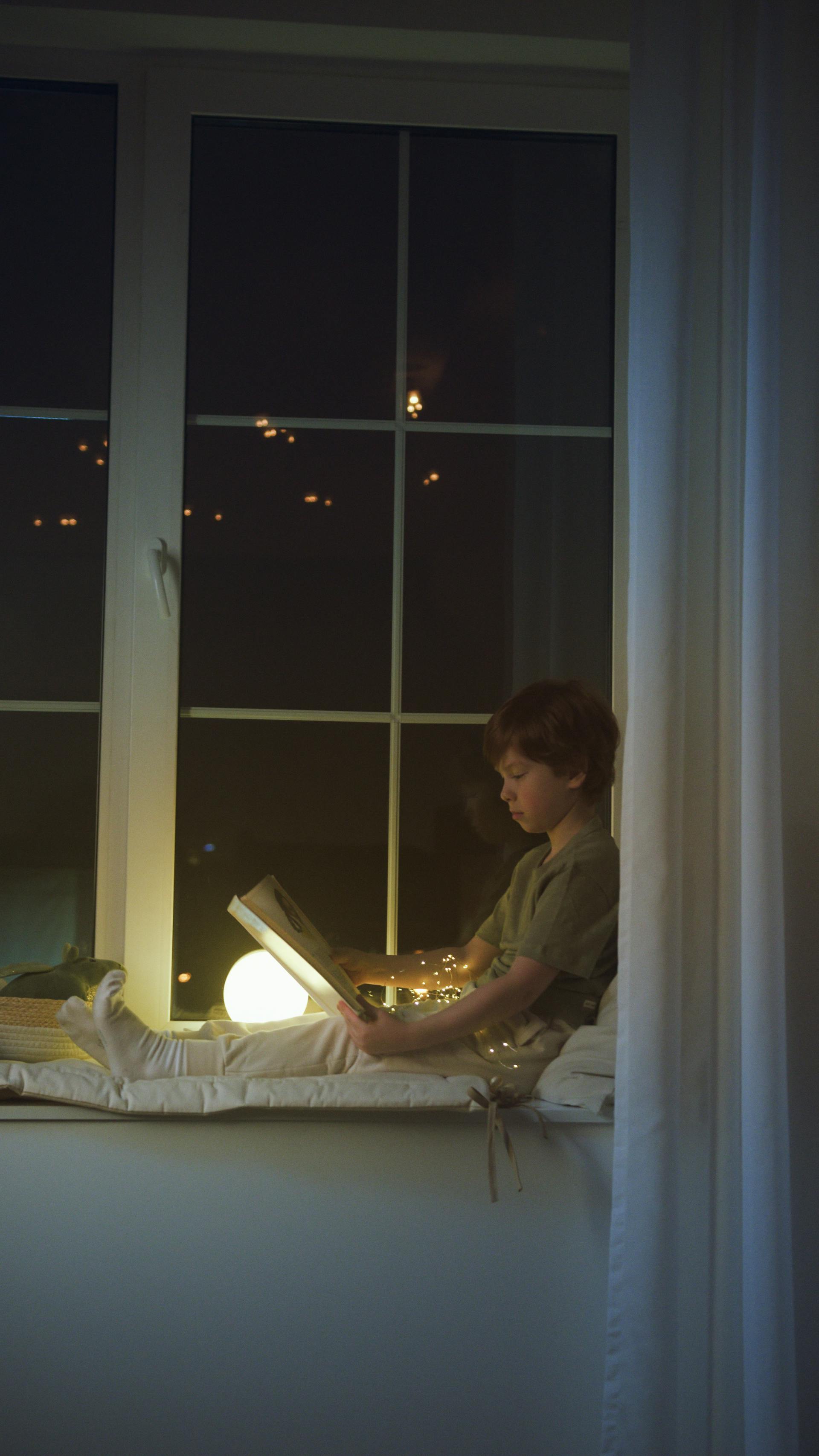 Un petit garçon lisant un livre assis sur le rebord d'une fenêtre | Source : Pexels