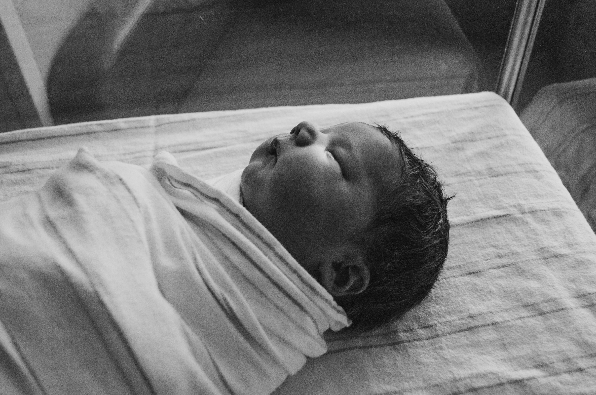 Photo en niveaux de gris d'un nouveau-né enveloppé dans un tissu | Source : Unsplash