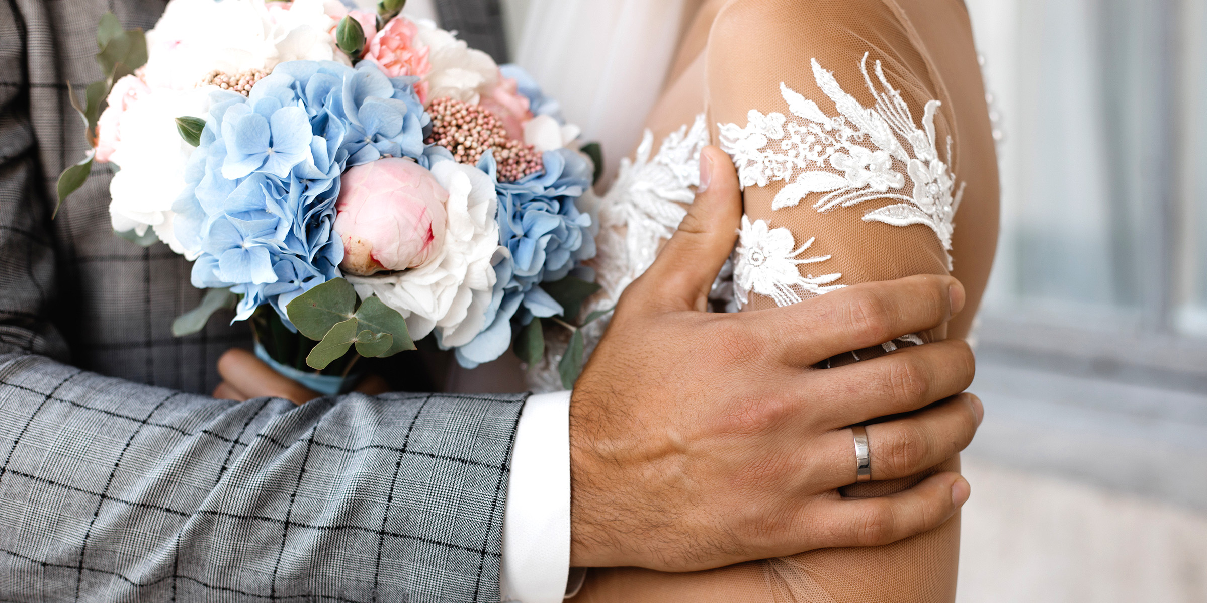 Un marié tient doucement sa fiancée, leurs mains s'enroulant autour d'un bouquet de fleurs pastel | Source : Freepik