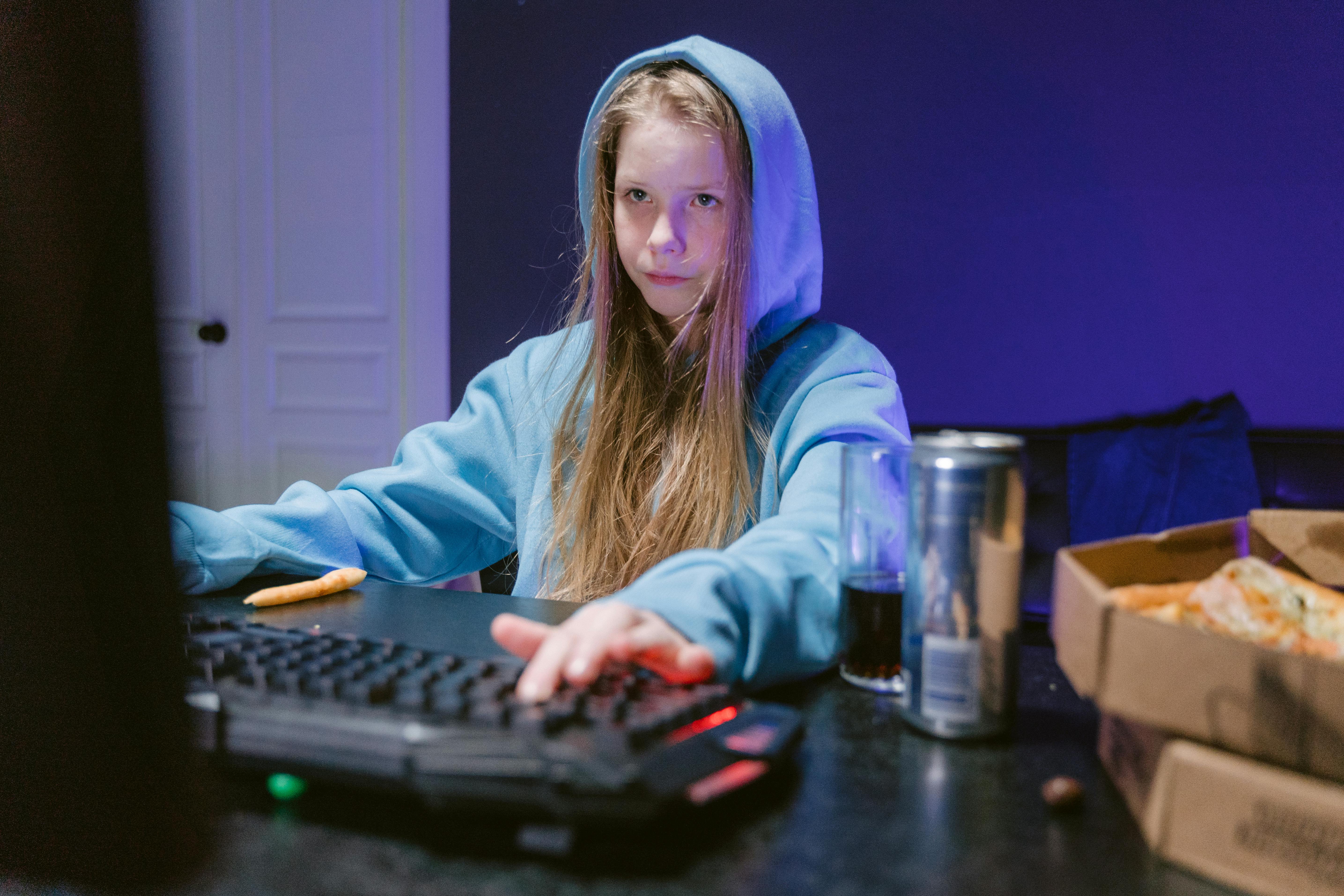 Une fille utilisant un ordinateur dans sa chambre avec des boissons et de la nourriture à portée de main | Source : Pexels