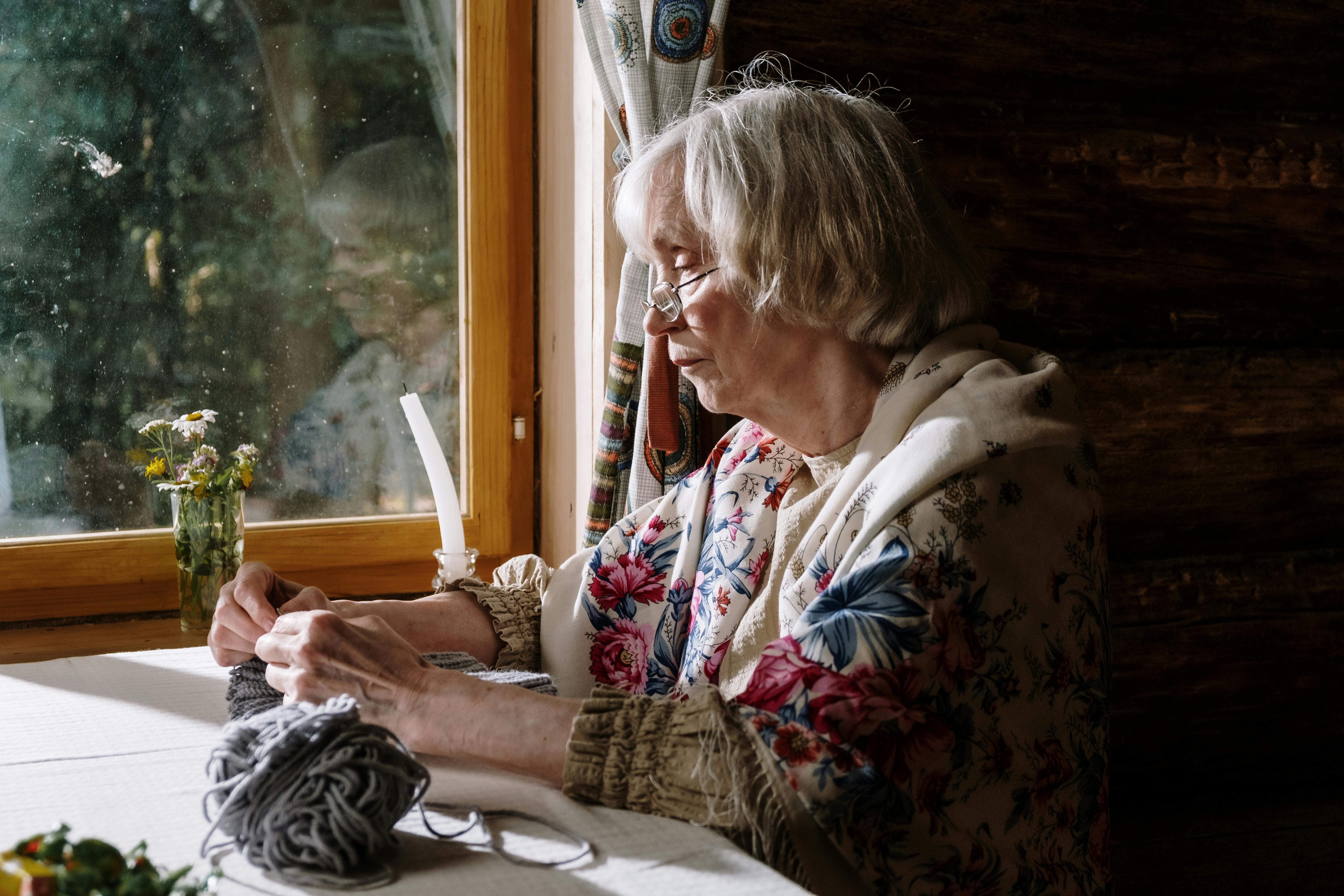 Mamie tricotant près de la fenêtre, fière et satisfaite | Source : Pexels