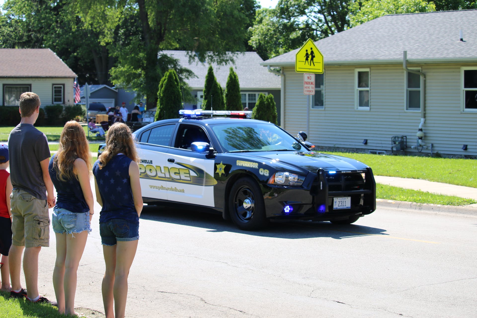 Des gens regardent une voiture de police qui passe dans un quartier | Source : Pexels