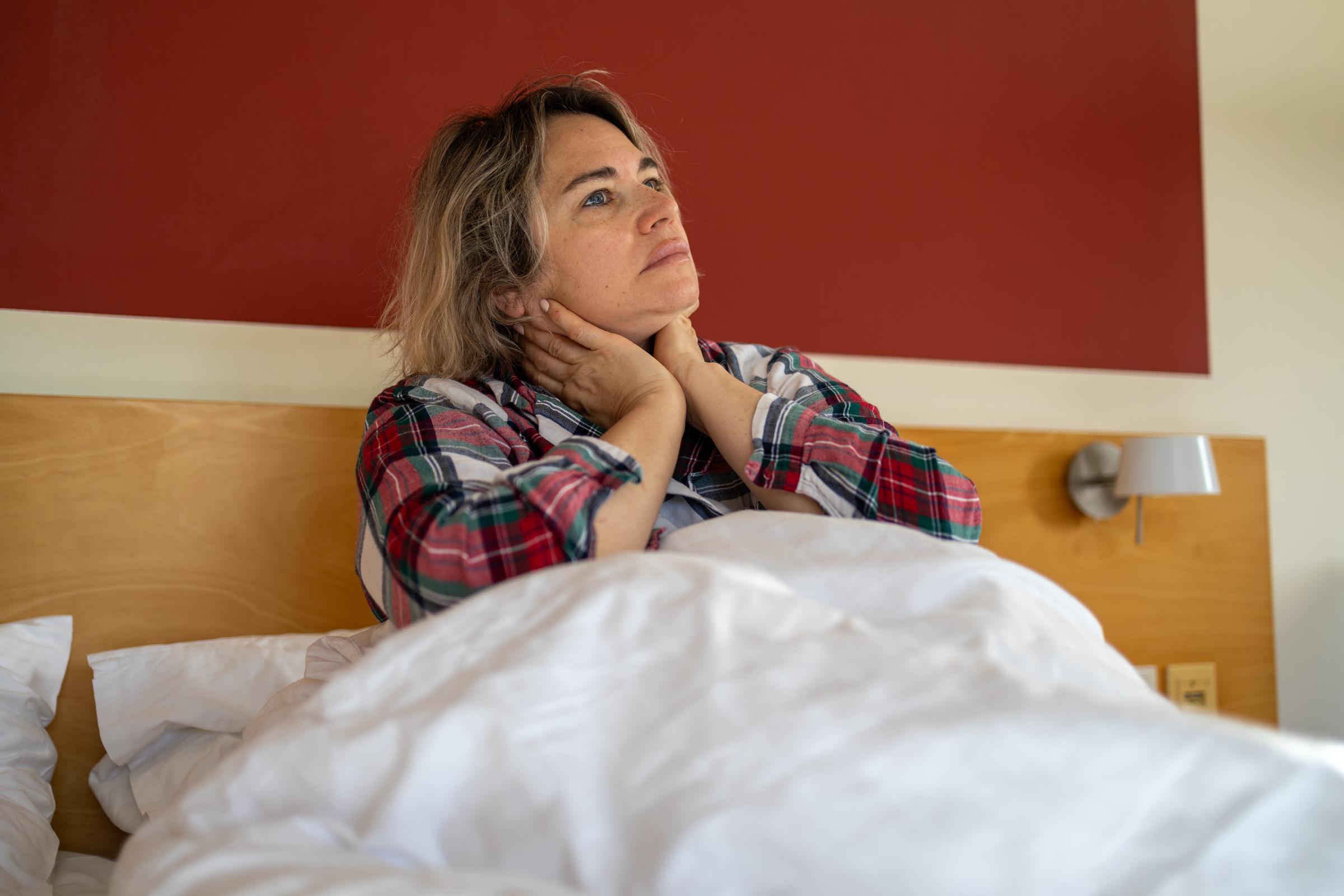 Femme fatiguée assise dans son lit, se tenant le cou en signe de douleur, symbolisant le stress, l'épuisement professionnel et les luttes pour la santé mentale | Source : Getty Images