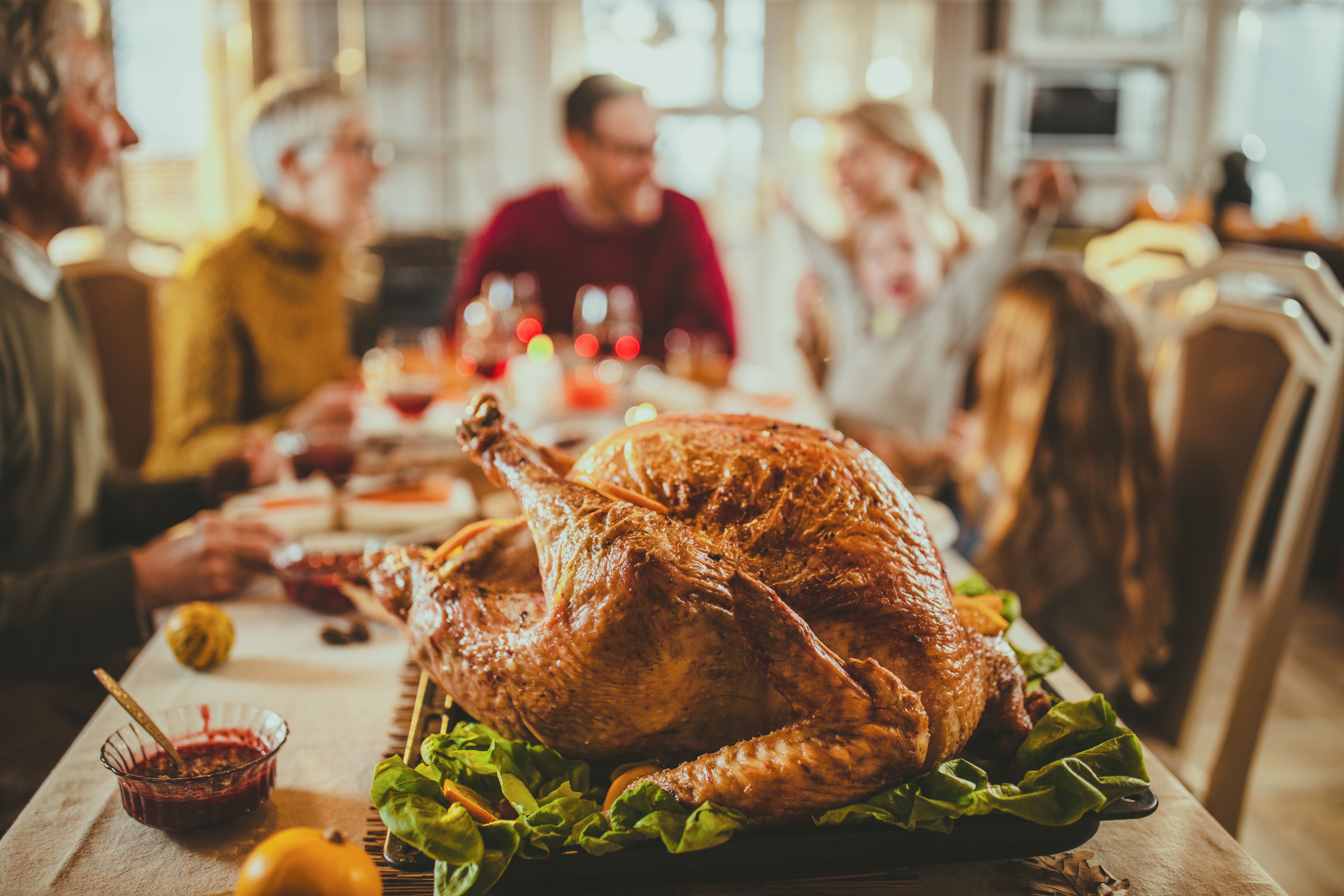 Dinde sur la table du dîner avec une famille derrière. | Source : Getty Images