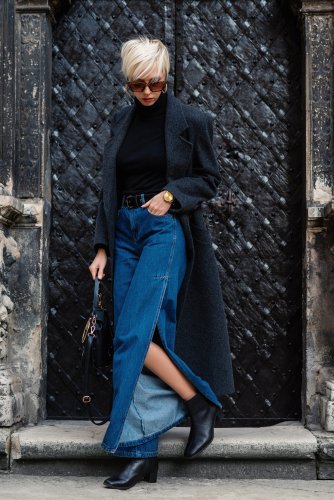 Femme à la mode portant un manteau gris de luxe, lunettes de soleil, jeans de coupe de jambes larges, bottes carrées pour chevilles, tenant un sac en cuir noir, posant sur les escaliers. | Photo : Getty Images
