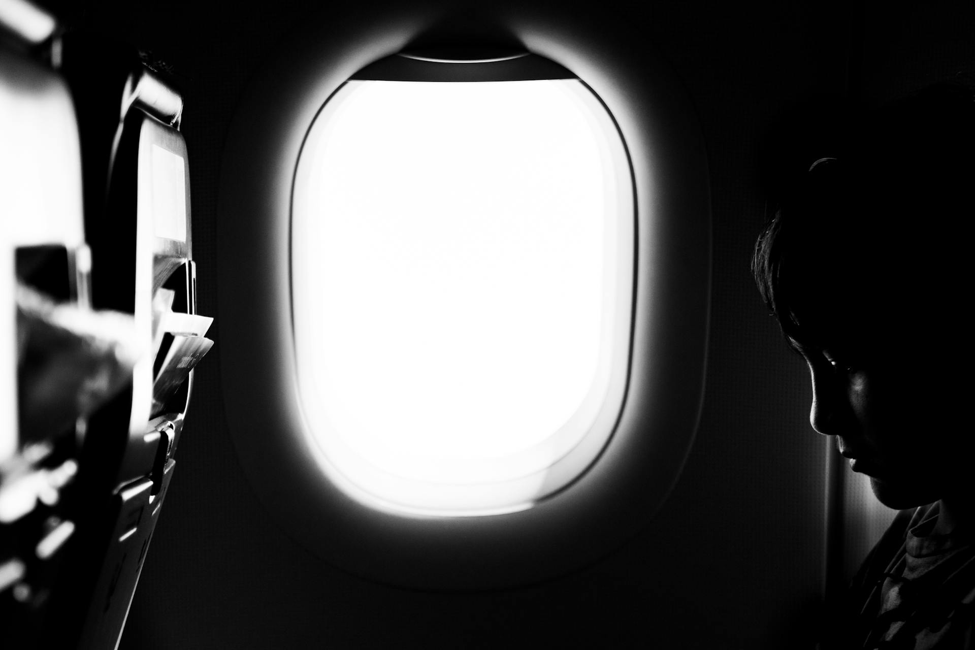 Grayscale photo of a boy sitting by the window on an airplane | Source: Pexels