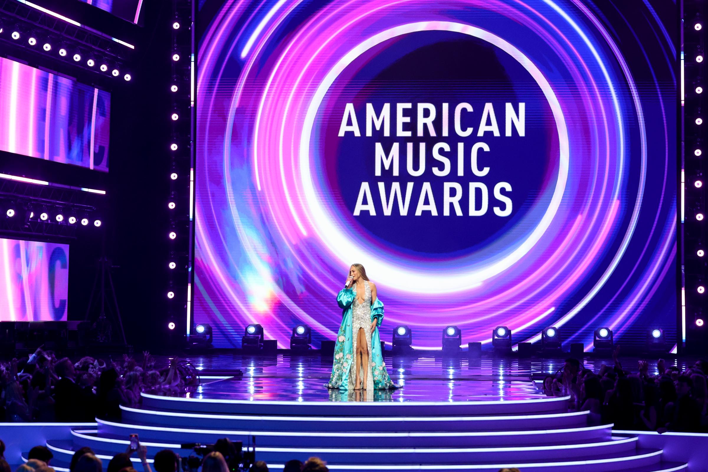 Dans un plan large de la scène éblouissante, la chanteuse de 55 ans est au centre de l'attention lors des American Music Awards, encadrée par des néons tourbillonnants sous le regard du public.