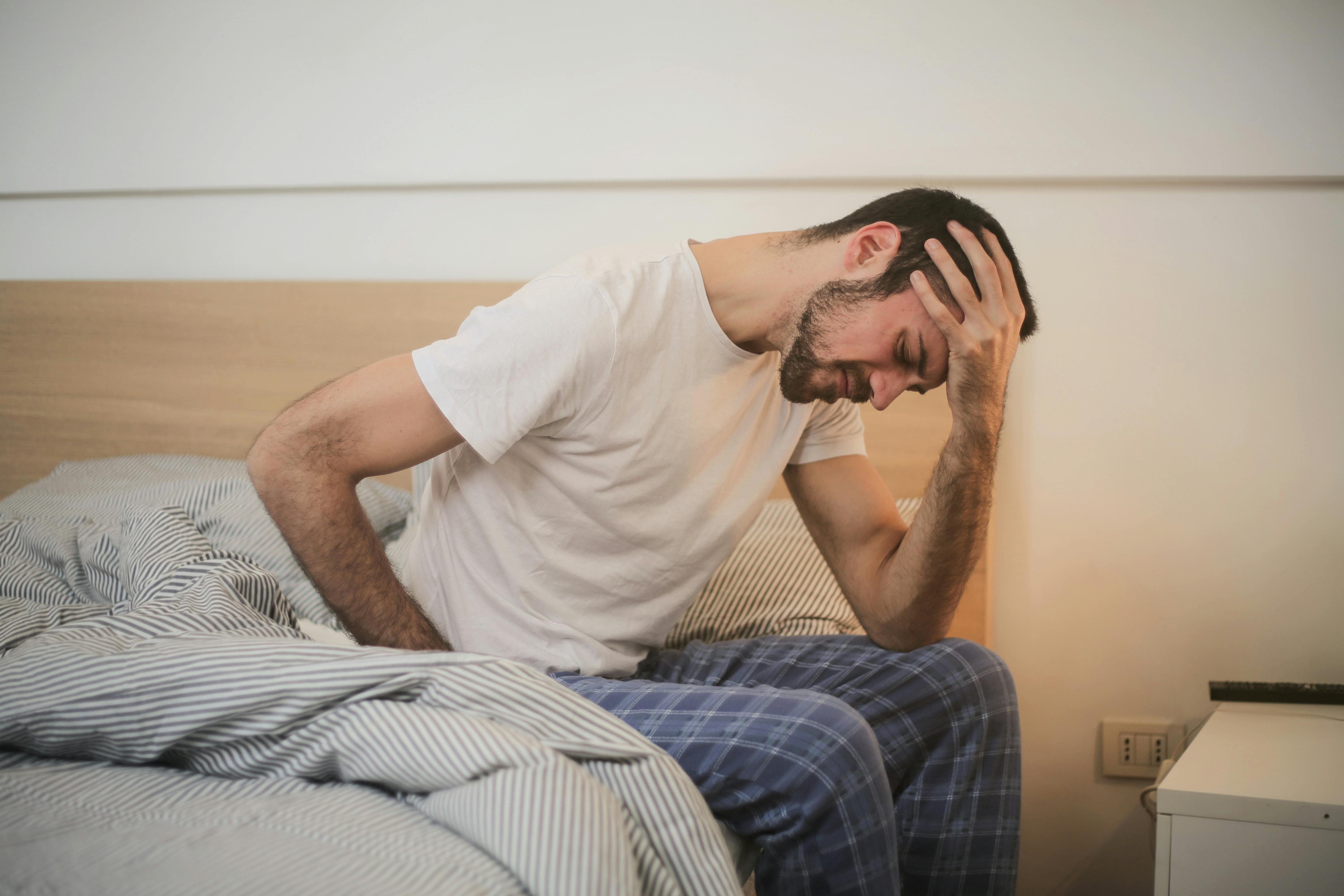 Un homme frustré assis sur son lit et se tenant la tête | Source : Pexels