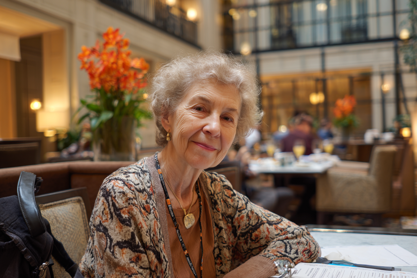 Une femme assise à une table dans un hôtel-restaurant sourit à quelqu'un | Source : Midjourney
