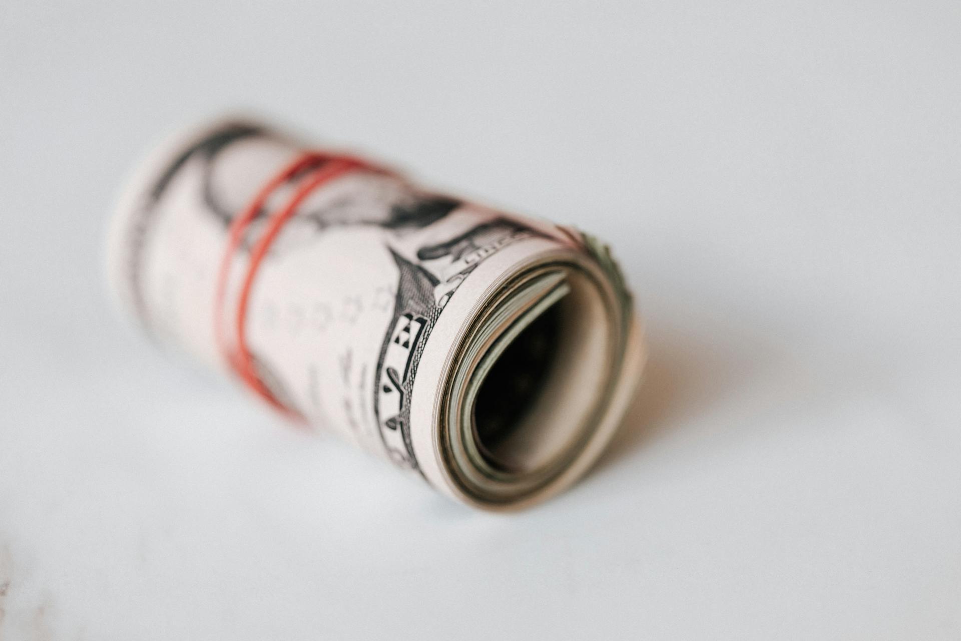 Un élastique rouge enroulé autour de billets de banque roulés | Source : Pexels