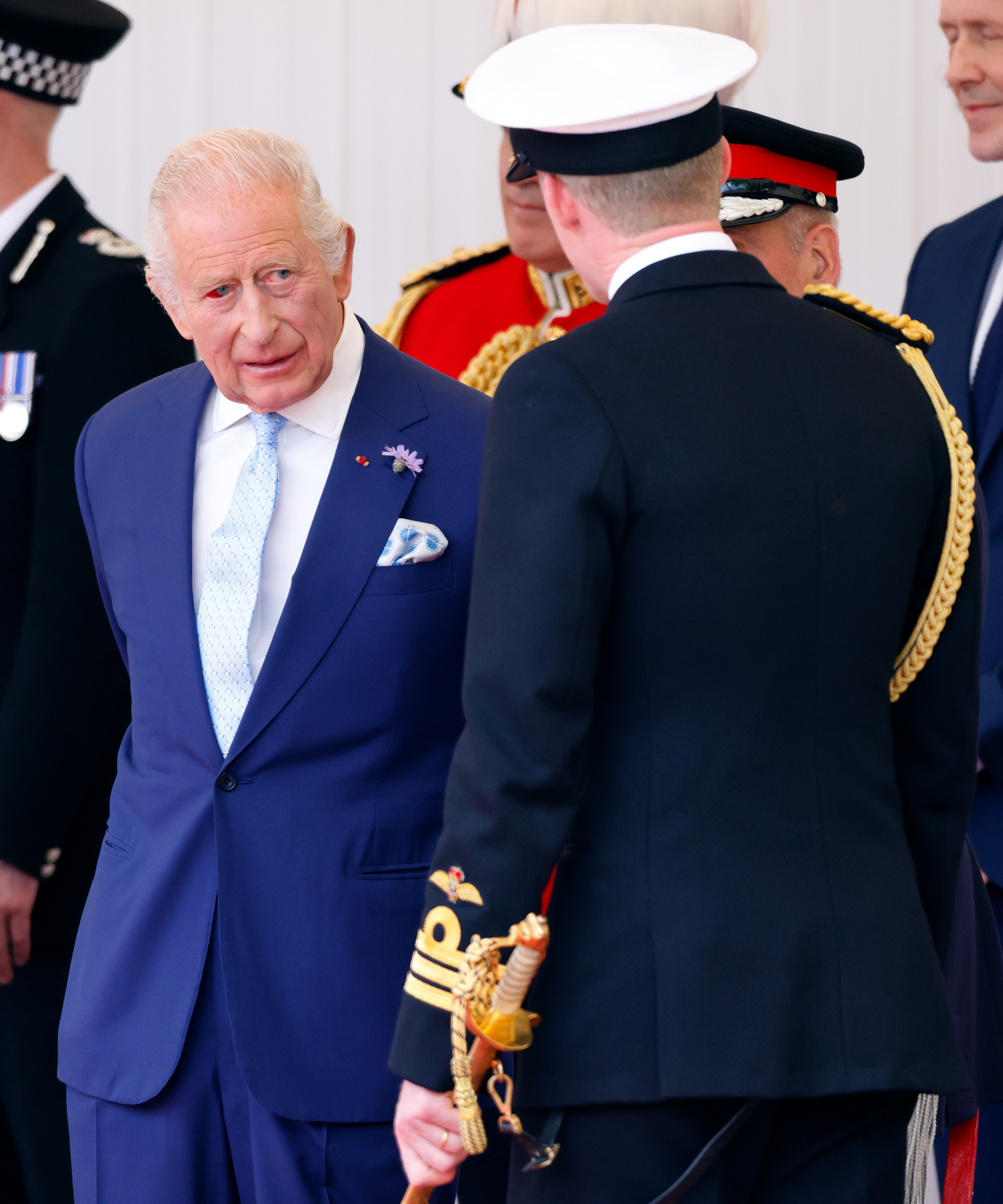 Le roi Charles III discute avec le personnel en uniforme lors de la cérémonie officielle de bienvenue à Windsor. Son œil rougi est faiblement visible alors qu'il s'acquitte de ses fonctions d'hôte avec l'aplomb qu'on lui connaît.