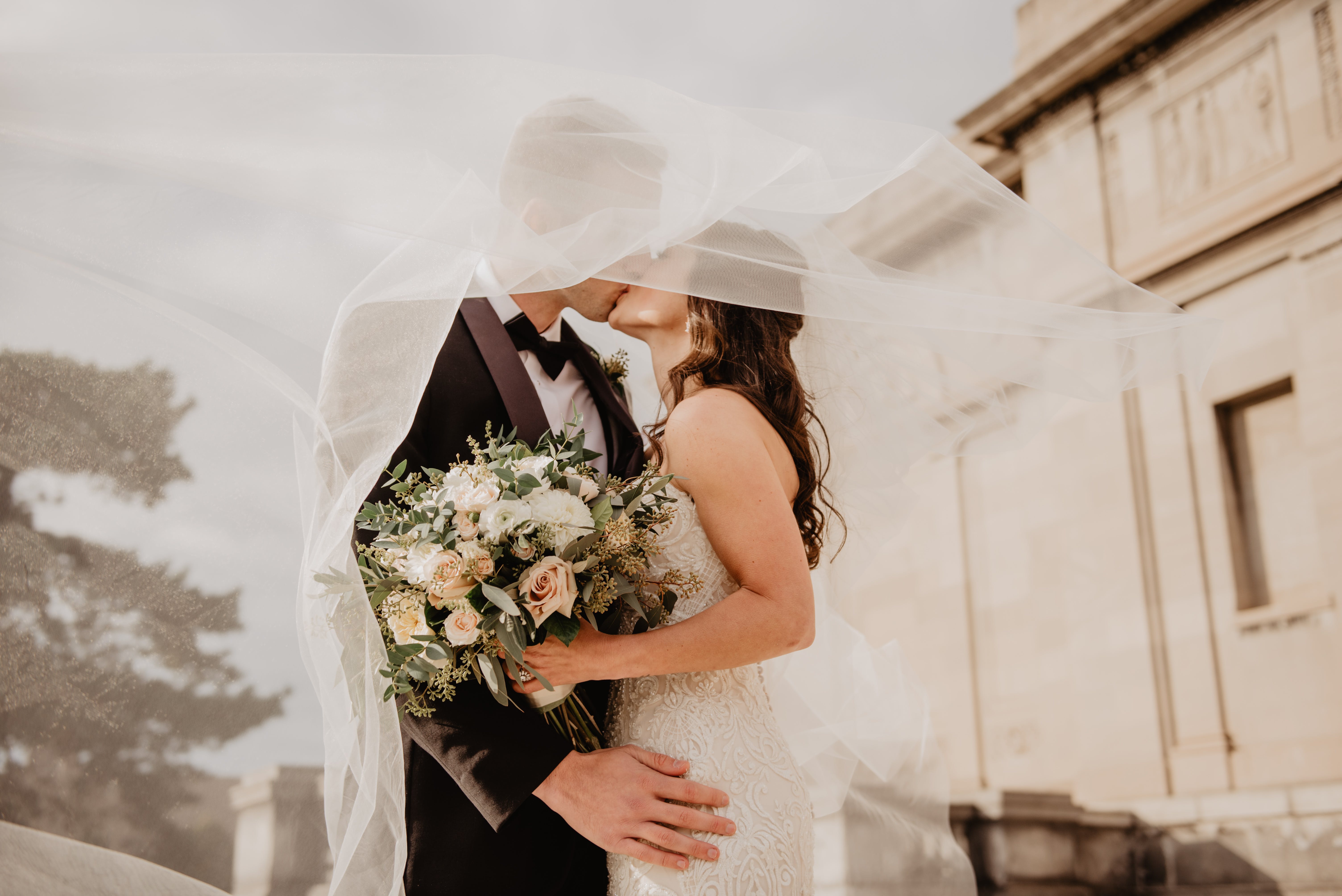 Un couple récemment marié s'embrassant sous le voile de la robe de mariée de la mariée | Source : Pexels