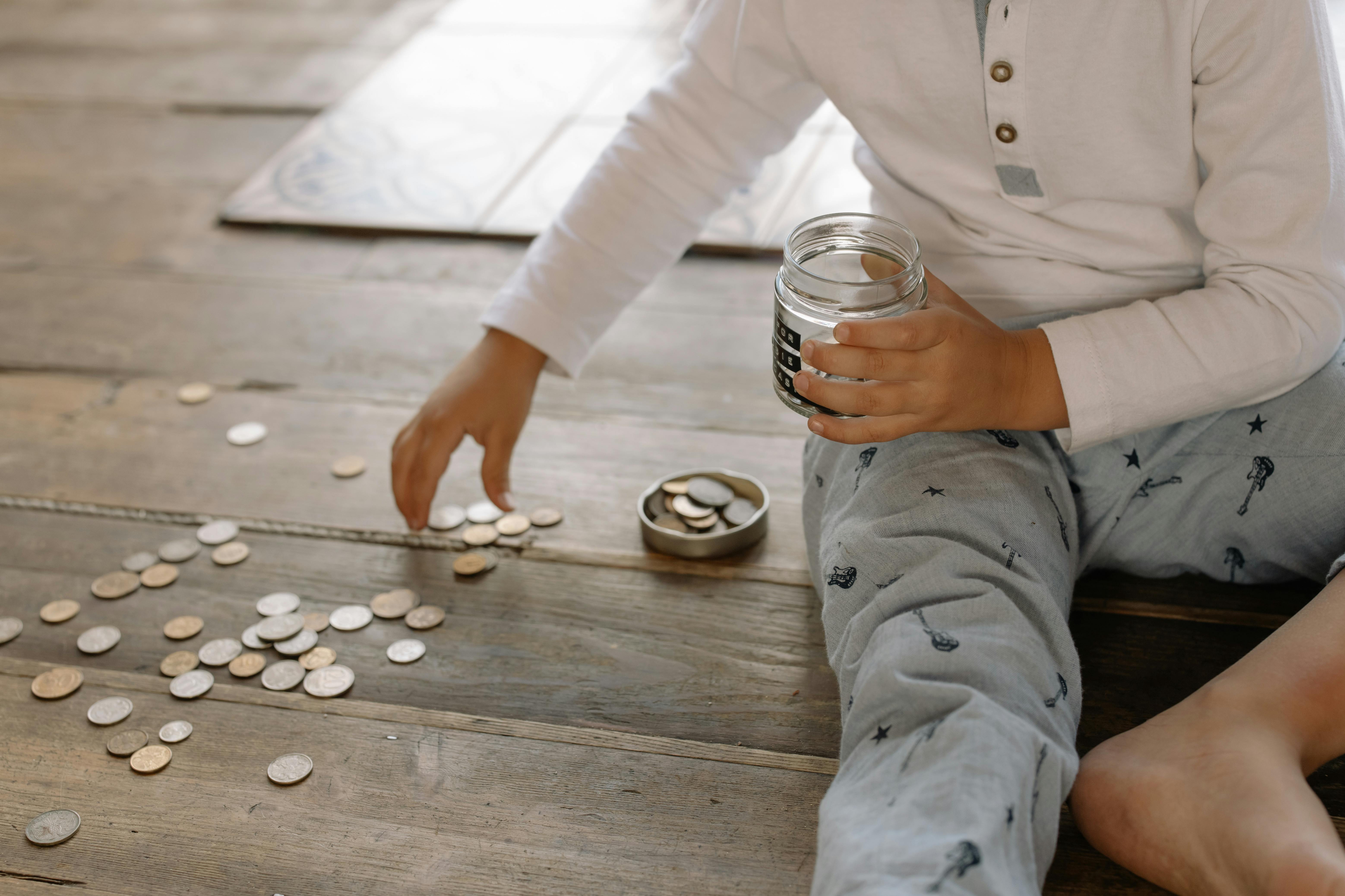 Un enfant mettant des pièces de monnaie dans un bocal en verre | Source : Pexels