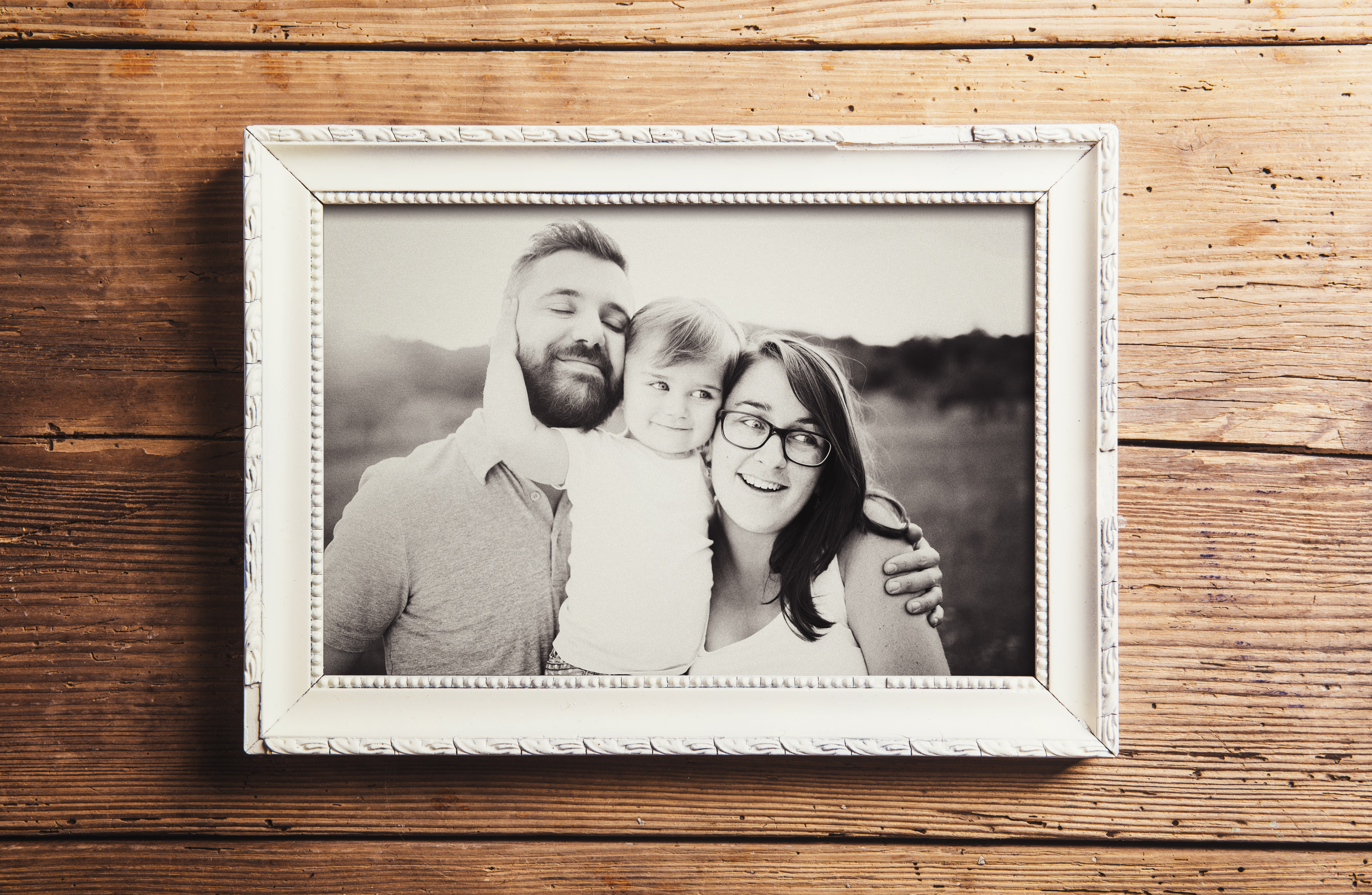 Une photographie en niveaux de gris d'une famille de trois personnes dans un cadre en bois | Source : Shutterstock