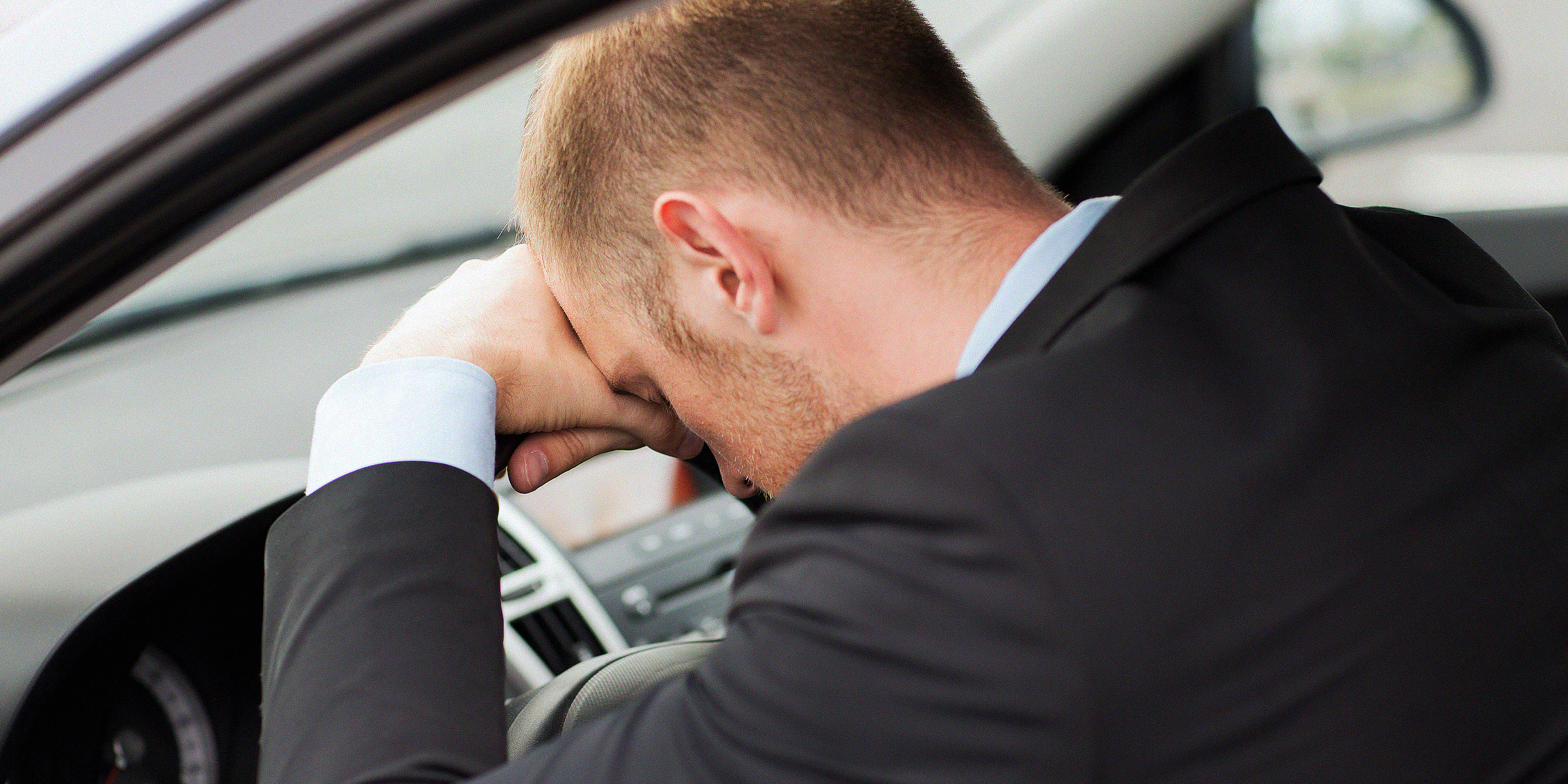 Un homme assis dans une voiture, la tête sur le volant | Source : Shutterstock