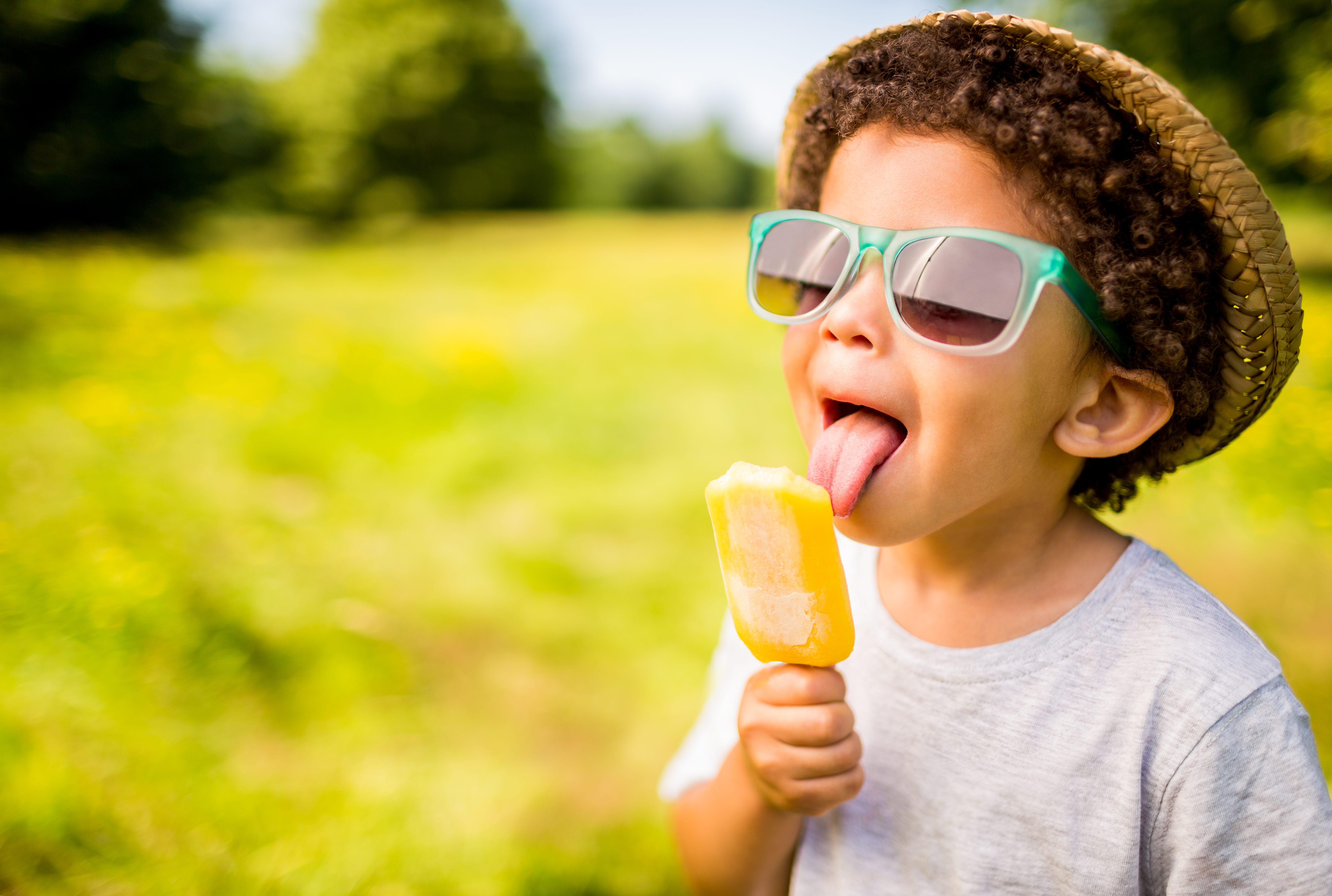 Garçon avec lunettes de soleil et chapeau mangeant une glace à l'extérieur | Source : Getty Images