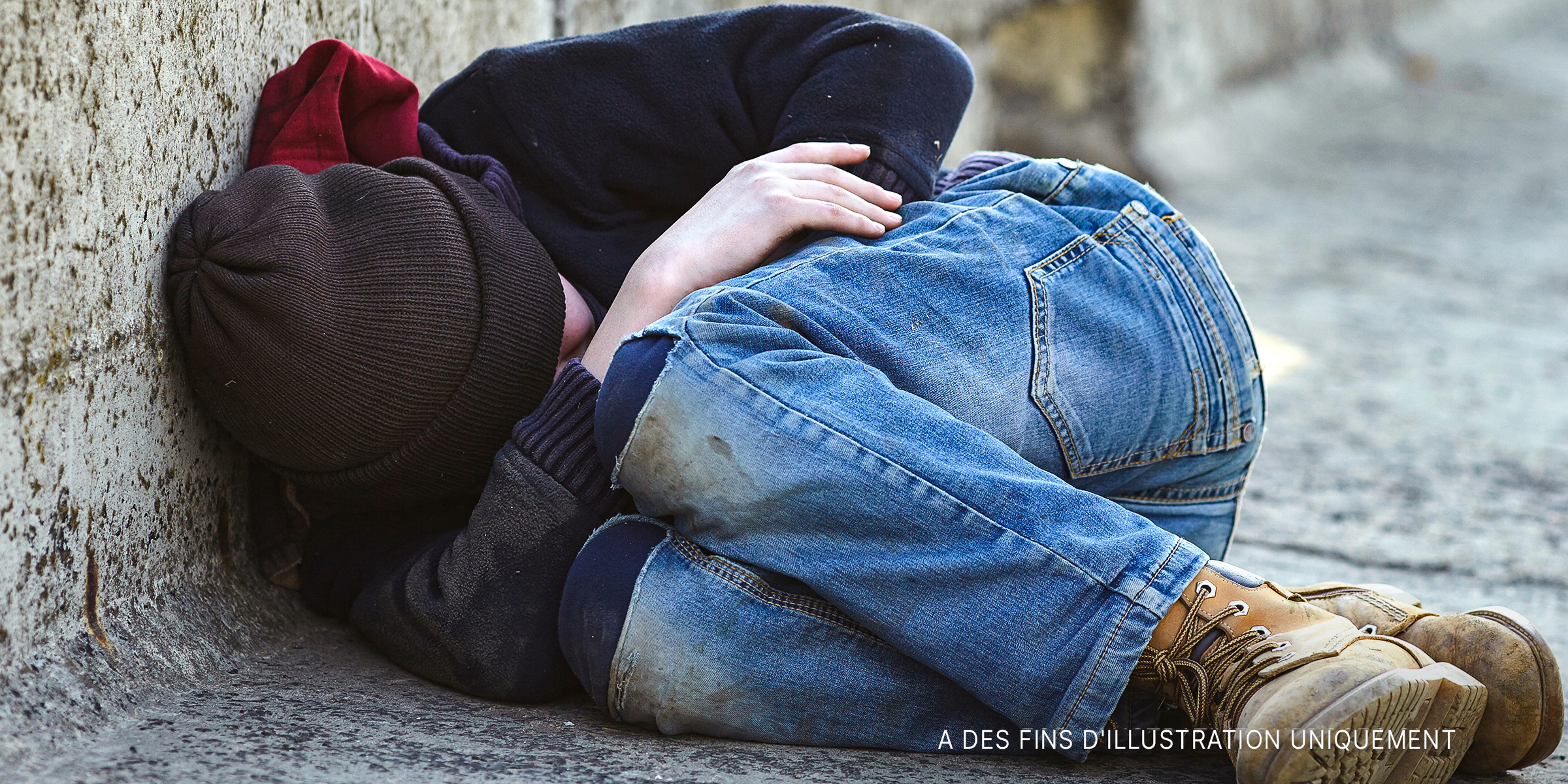 Un jeune garçon se recroqueville en dormant dans la rue | Source : Shutterstock