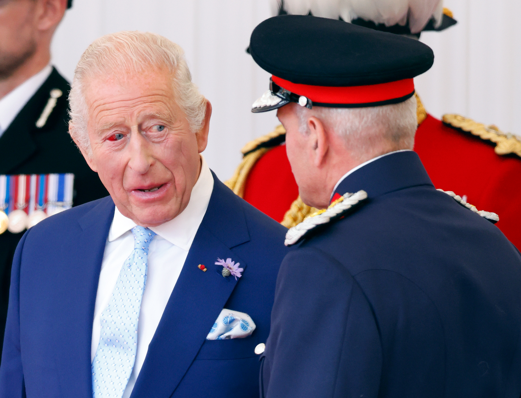 Un gros plan du roi Charles III révèle la teinte rouge de son œil droit alors qu'il converse avec un homme en uniforme. Malgré l'éclatement du vaisseau, le roi reste engagé tout au long de l'accueil officiel.