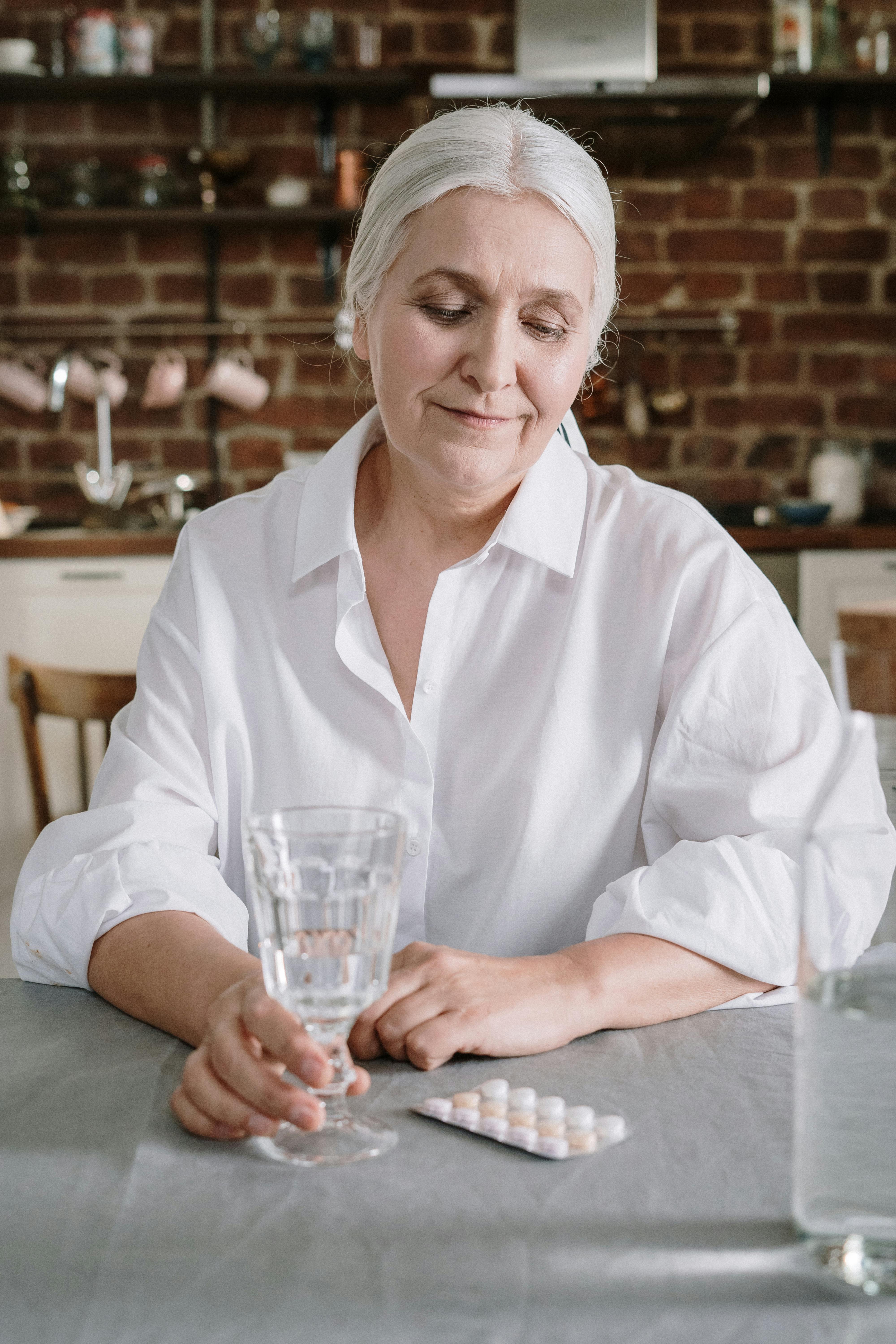 Une femme âgée assise à la table, regardant un ensemble de médicaments | Source : Pexels