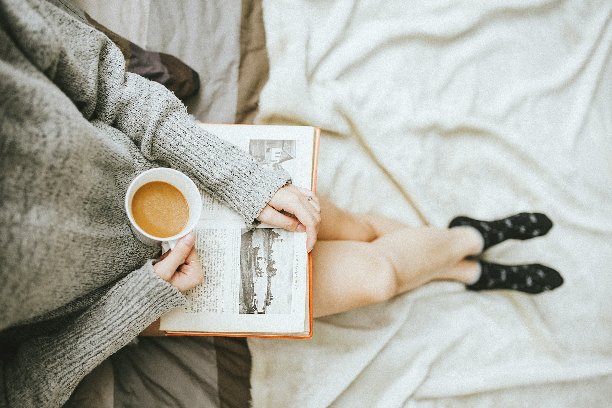 Une femme lisant un livre tout en savourant une tasse de café à la maison | Source : Unsplash