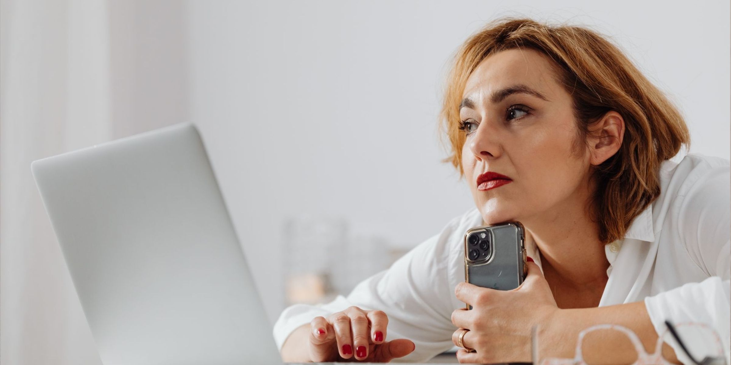 Une femme à l'air triste tenant son téléphone tout en utilisant un ordinateur portable | Source : Pexels