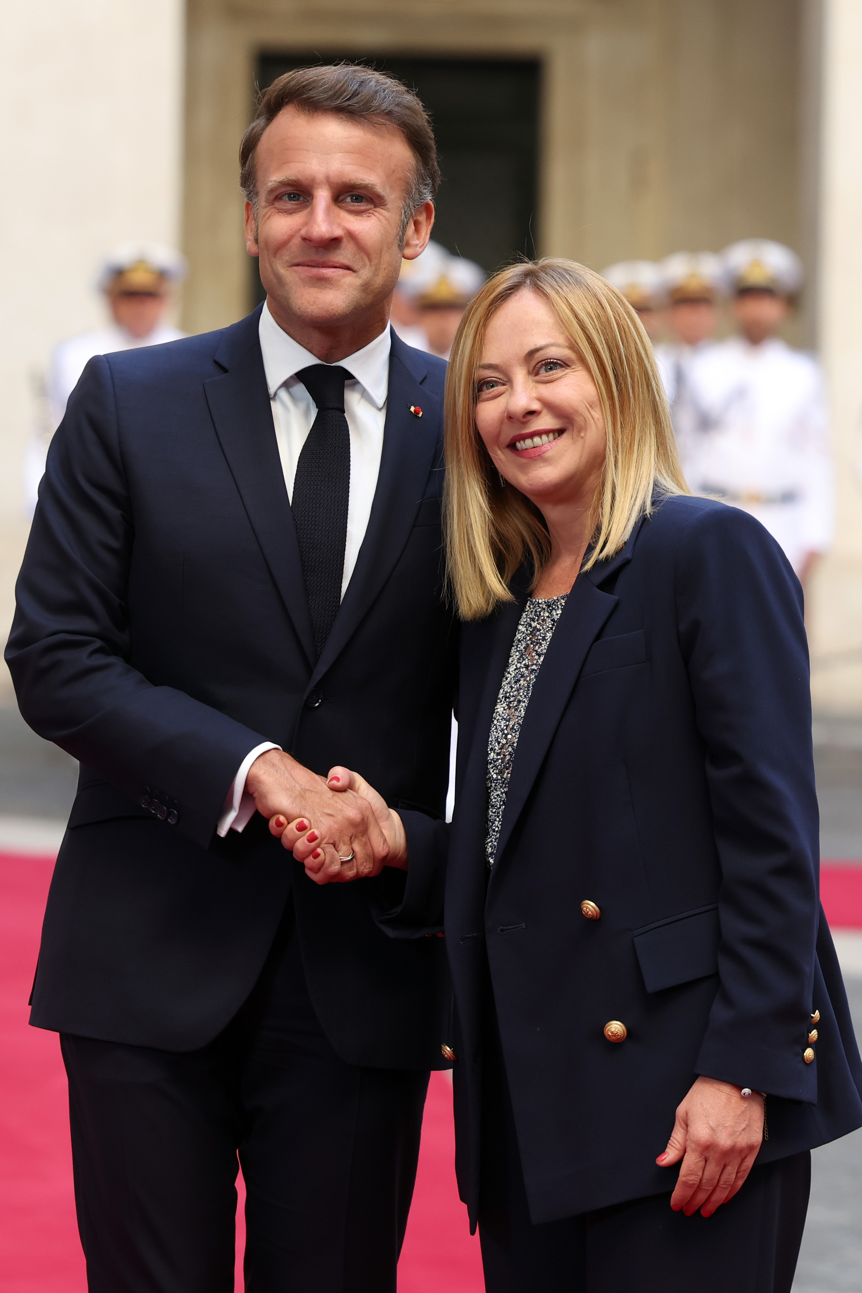 Emmanuel Macron et Giorgia Meloni posent côte à côte devant le Palazzo Chigi, souriant chaleureusement en se serrant la main. Le moment capture un échange formel mais amical entre les deux dirigeants.