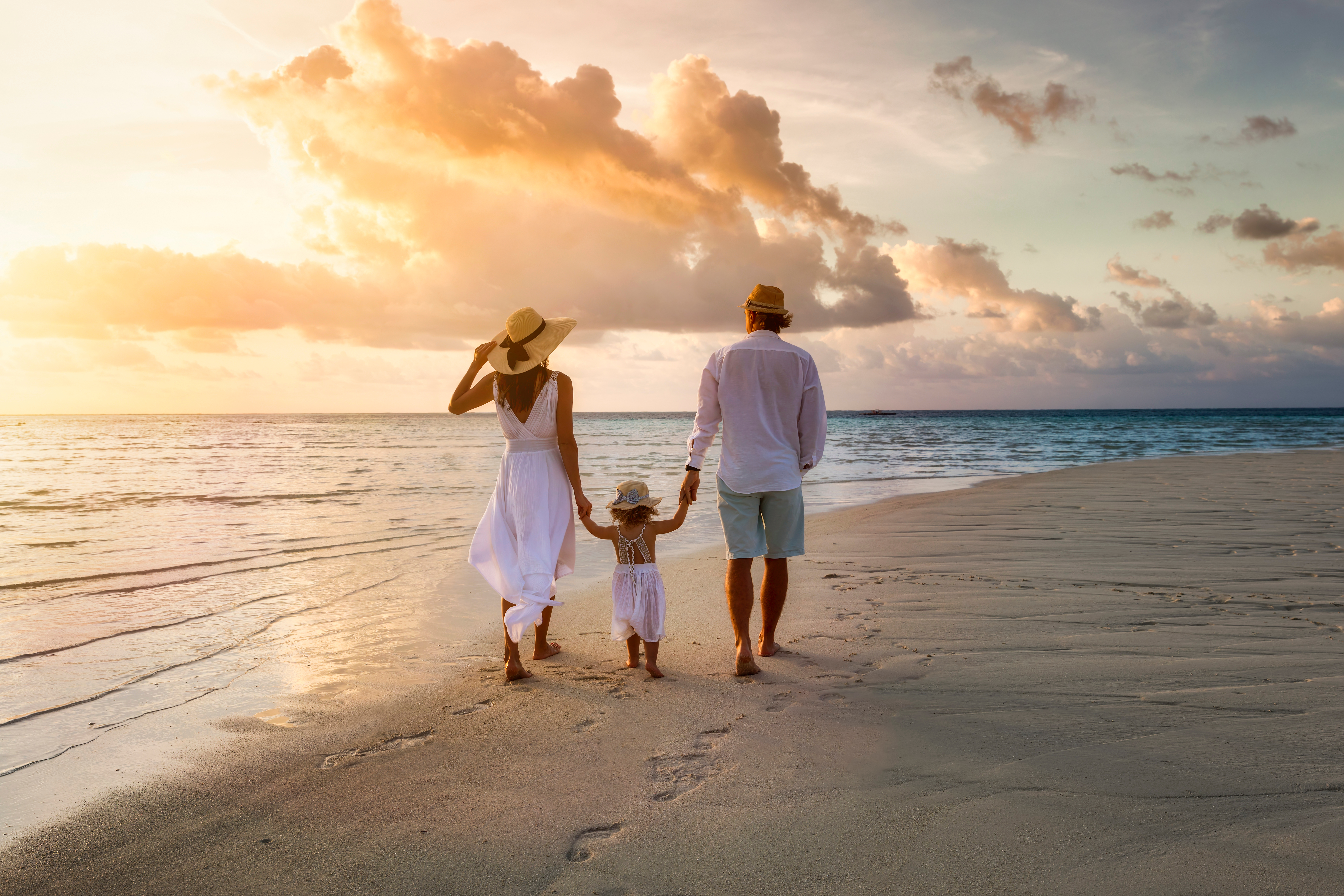 Une famille élégante en vêtements d'été blancs marchant main dans la main sur une plage paradisiaque tropicale pendant le coucher du soleil | Source : Shutterstock