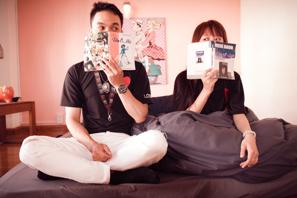 Un couple assis sur un lit et tenant des livres. | Photo : Pexels