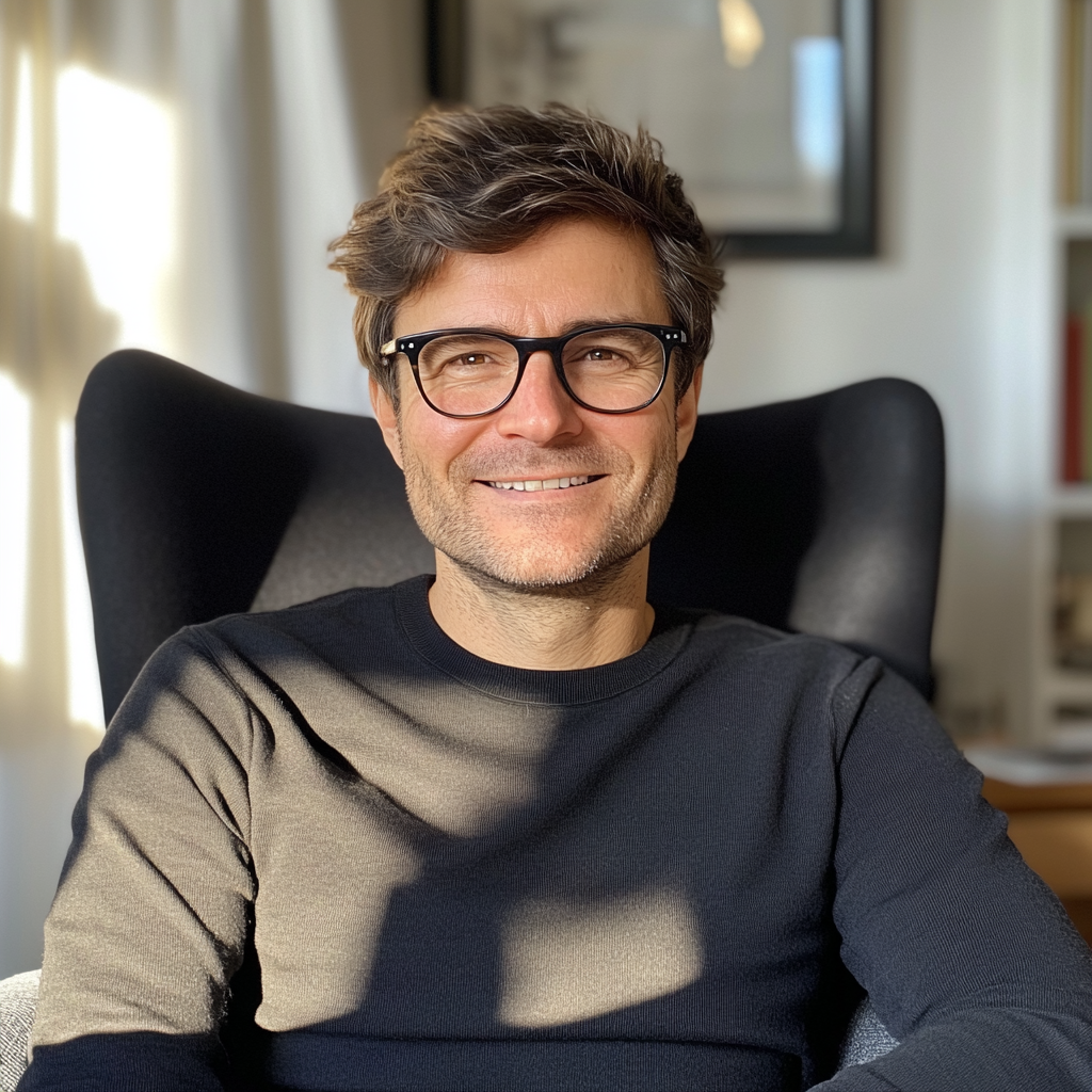 Un homme souriant portant un pull noir et assis dans un fauteuil | Source : Midjourney